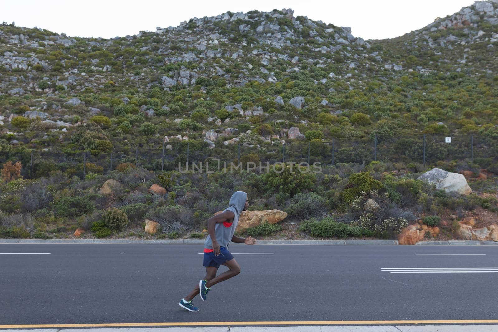 Fit african american man in sportswear running on a coastal road. healthy lifestyle, exercising in nature.