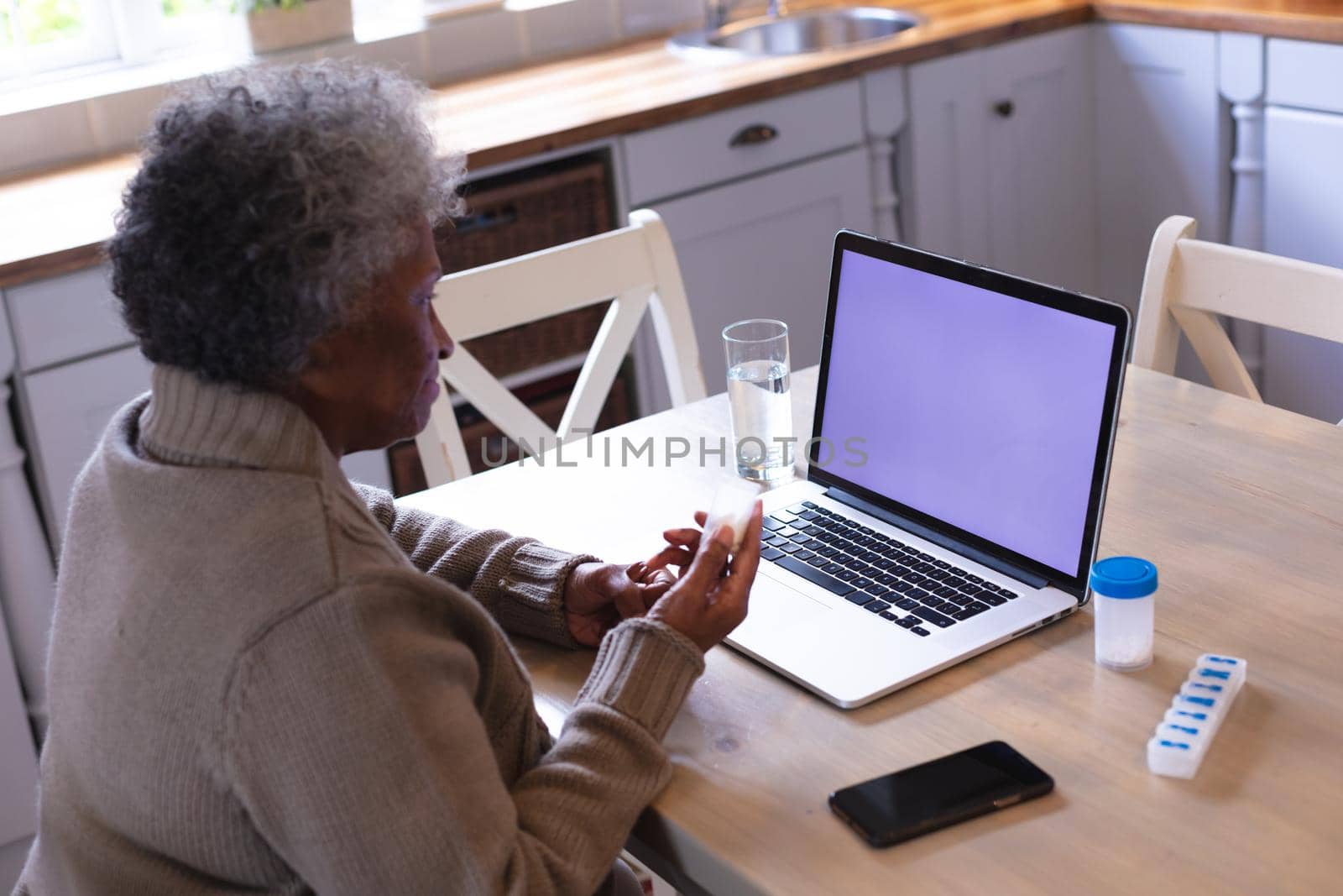 African american senior woman holding empty medication container while having a videocall on laptop at home. distant communication and telemedicine consultation concept.