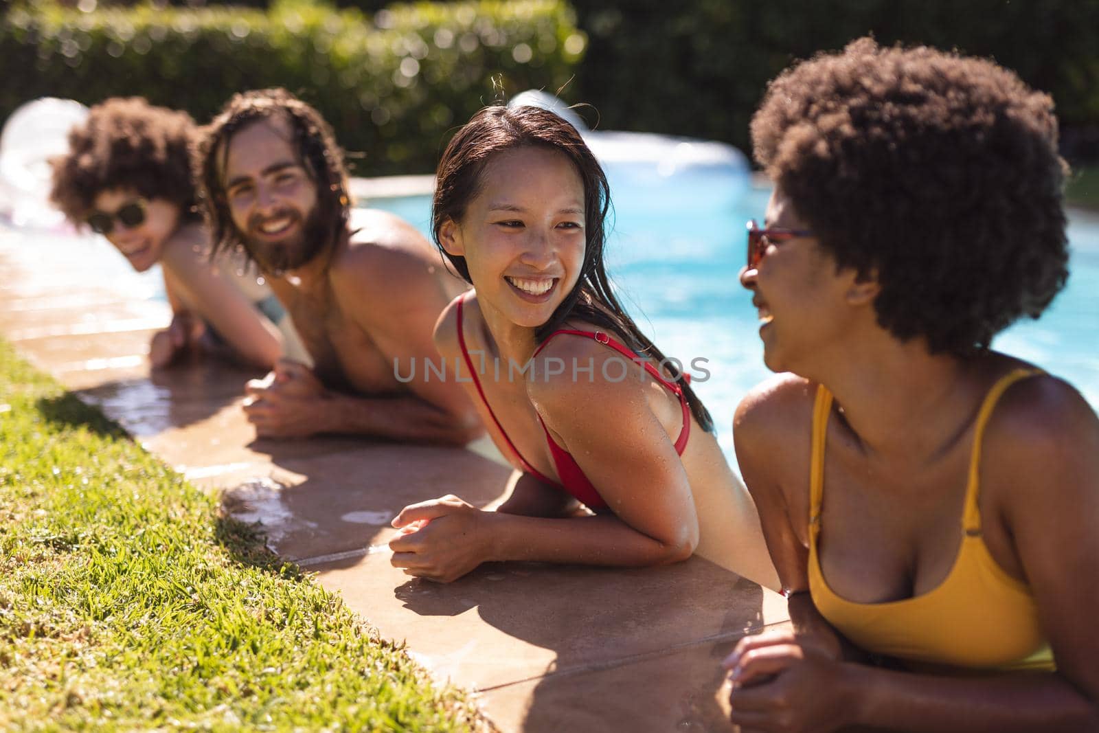 Diverse group of friends smiling and leaning on the poolside by Wavebreakmedia