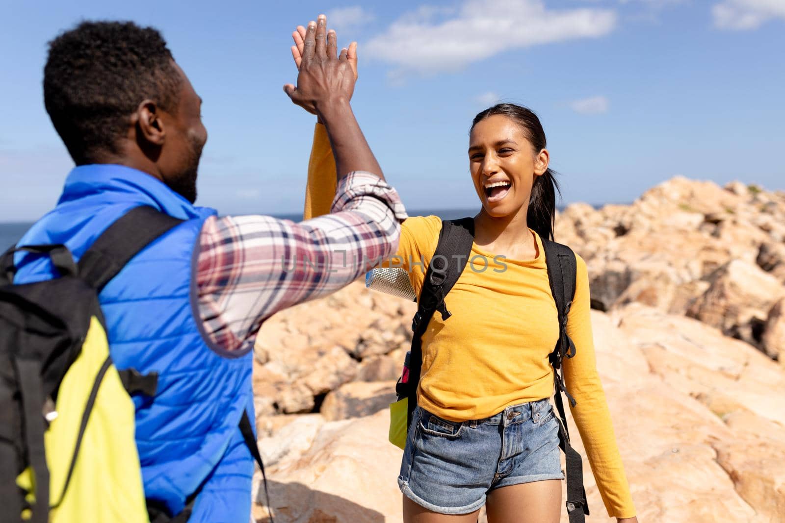 Fit afrcan american couple wearing backpacks high fiving hiking on the coast. healthy lifestyle, exercising in nature.