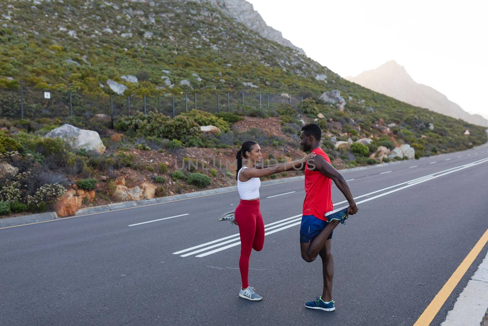 Fit african american couple in sportswear stretching on a coastal road. healthy lifestyle, exercising in nature.