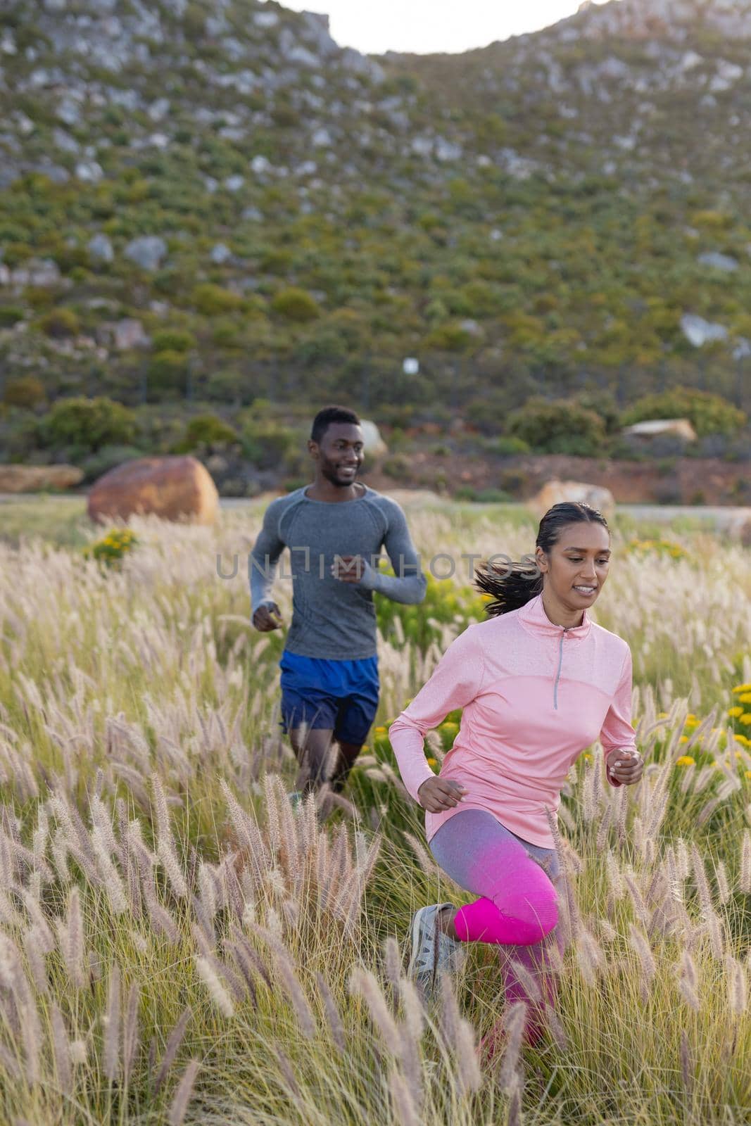 Fit african american couple in sportswear running through tall grass. healthy lifestyle, exercising in nature.