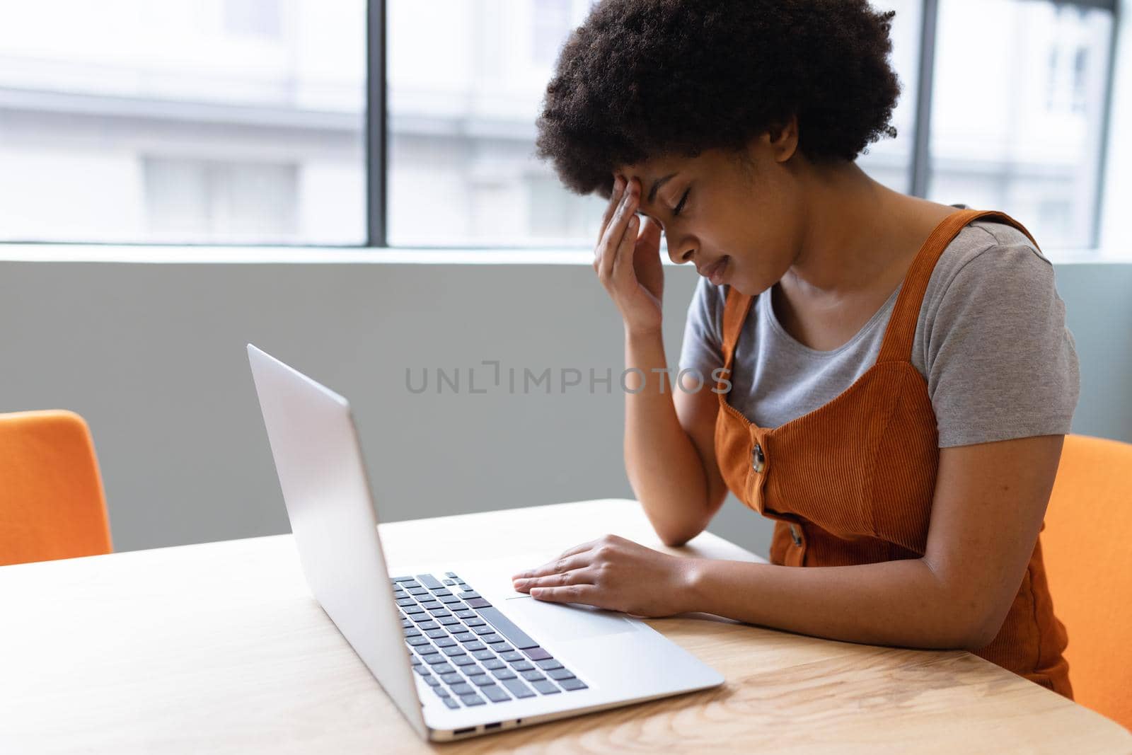 Mixed race businesswoman working in creative office. woman sitting at table and using laptop. social distancing in workplace during covid 19 pandemic.