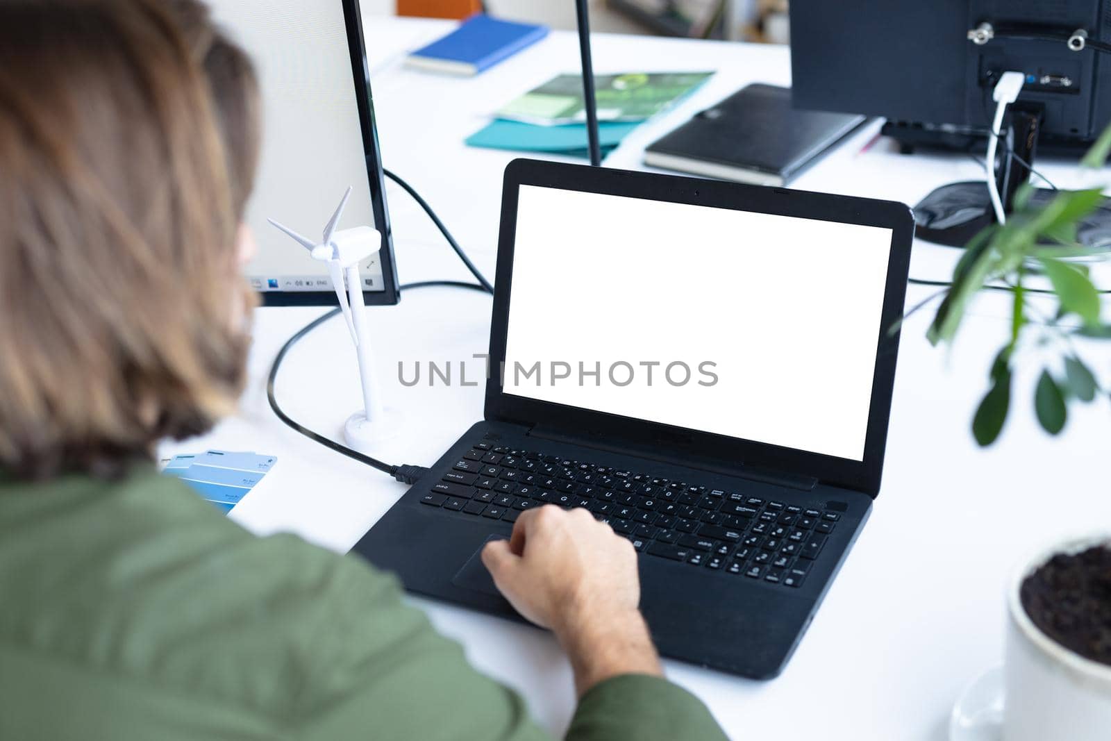 Caucasian businessman sitting at desk using laptop computer in creative office. social distancing in workplace during covid 19 pandemic.