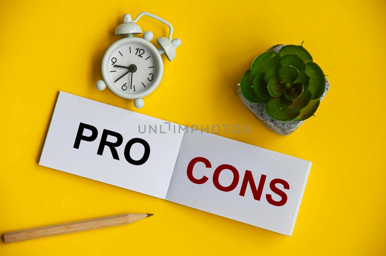 Pro and cons text on notepad with alarm clock and plant on yellow background.