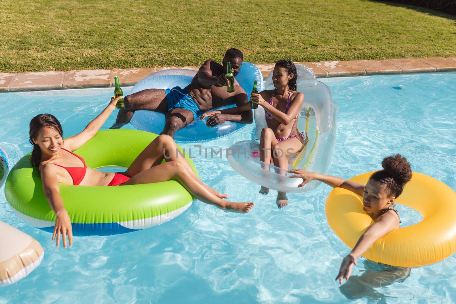 Diverse group of friends having fun playing on inflatables in swimming pool by Wavebreakmedia