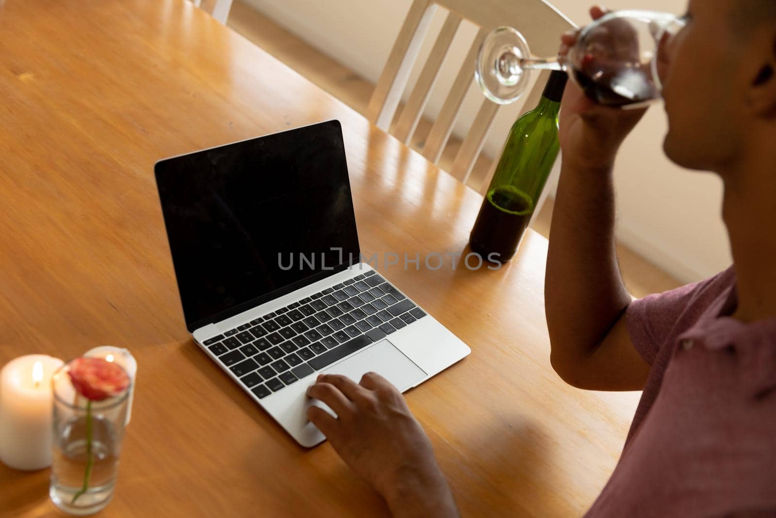 Mixed race man sitting at table making video call and drinking wine. staying at home in isolation during quarantine lockdown.