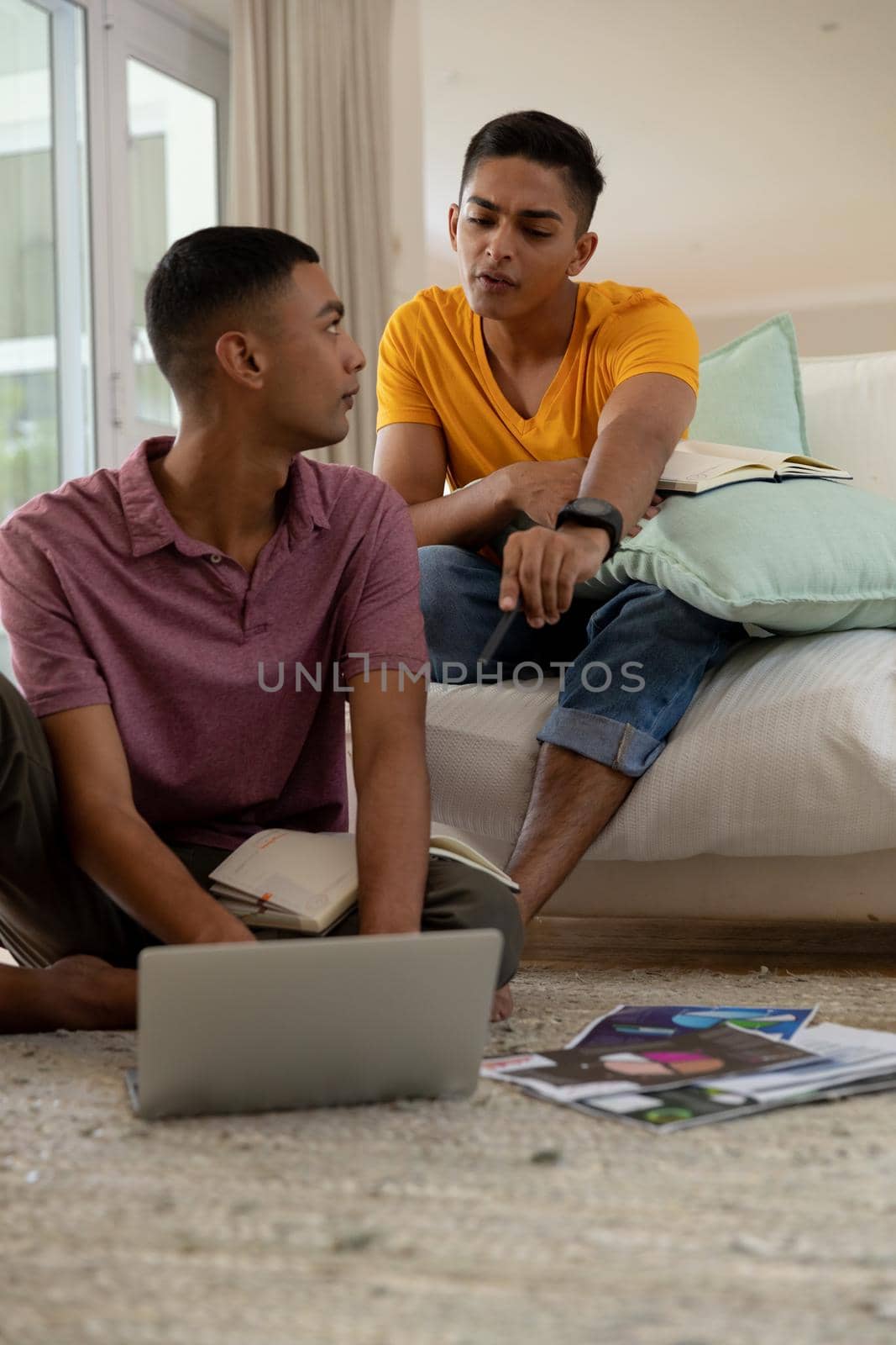 Diverse gay male couple sitting in living room using laptop and learning. staying at home in isolation during quarantine lockdown.