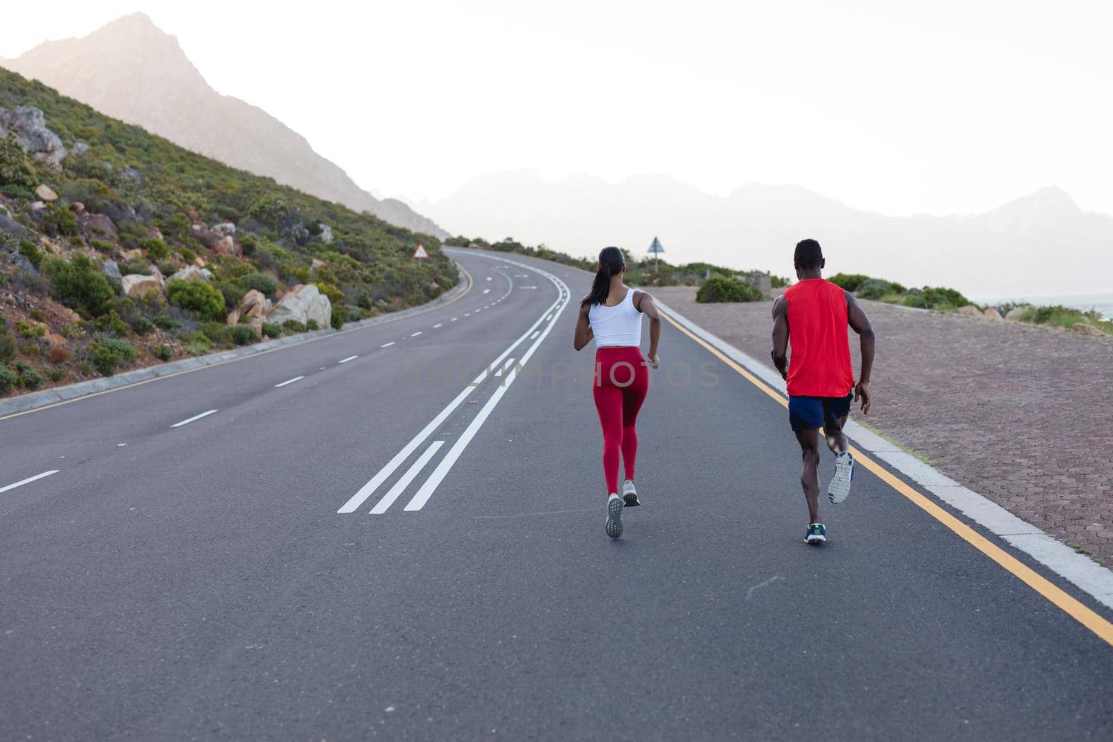 Fit african american couple in sportswear running on a coastal road. healthy lifestyle, exercising in nature.