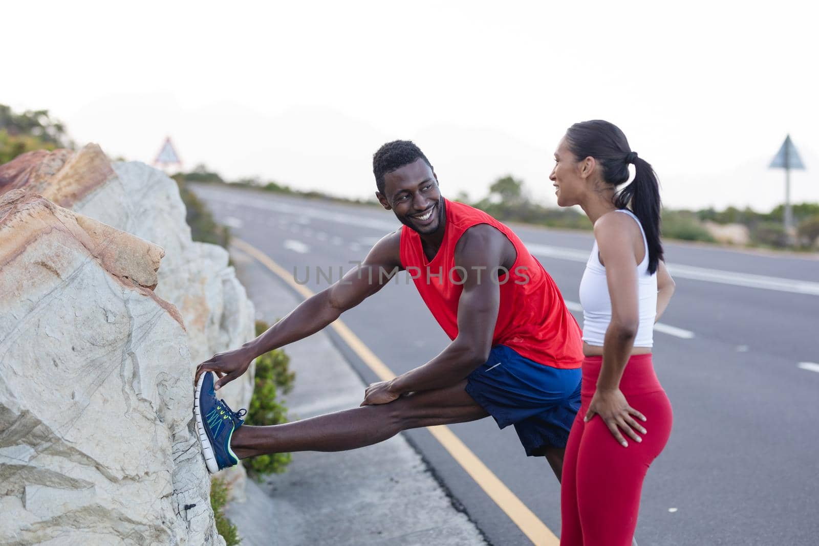 Fit african american man in sportswear stretching while woman is standing on a coastal road by Wavebreakmedia