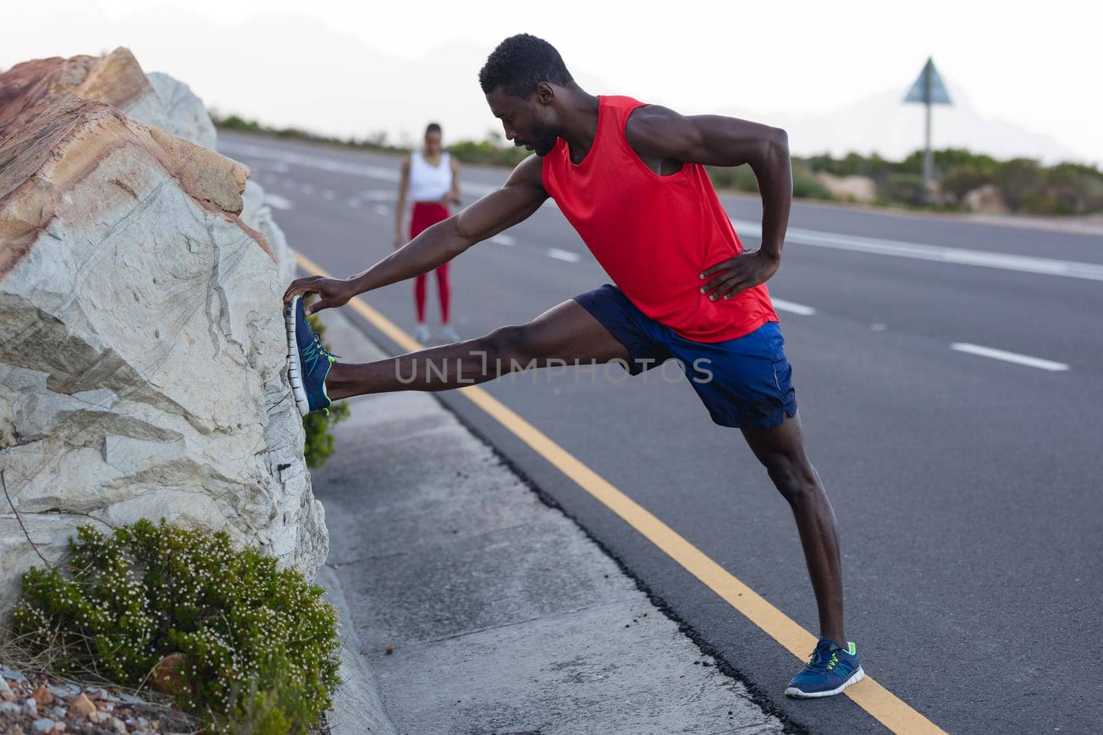 Fit african american man in sportswear stretching on a coastal road. healthy lifestyle, exercising in nature.