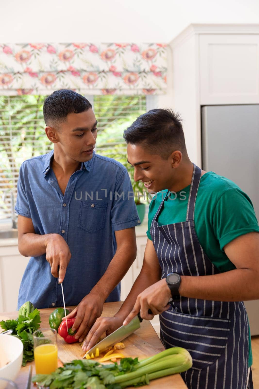 Diverse gay male couple spending time in kitchen cooking together and smiling. staying at home in isolation during quarantine lockdown.