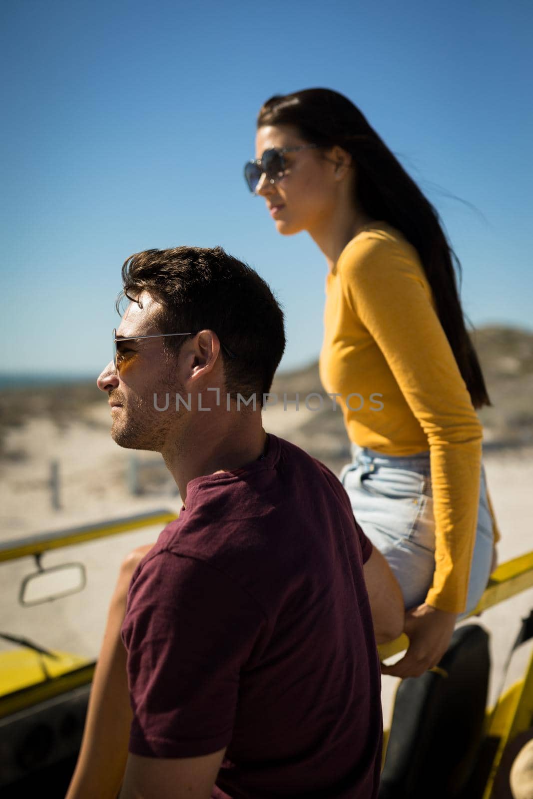 Happy caucasian couple in beach buggy by the sea looking ahead wearing sunglasses. beach break on summer holiday road trip.