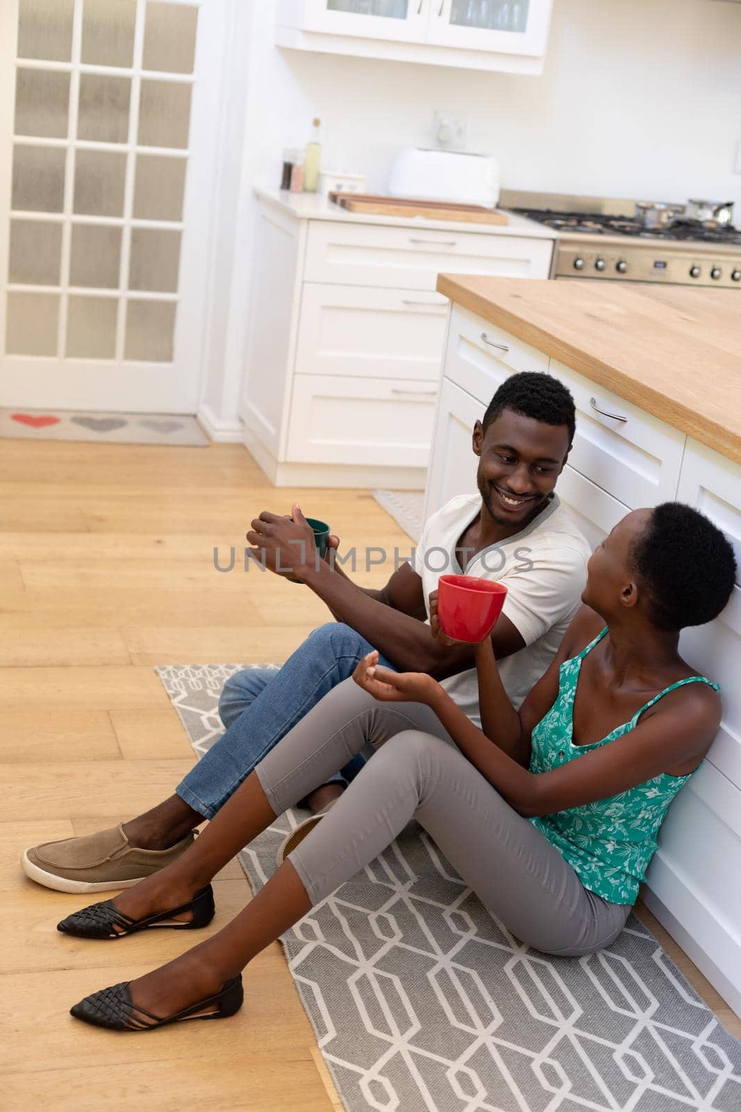 African american couple sitting on floor in kitchen holding mugs. staying at home in isolation during quarantine lockdown.