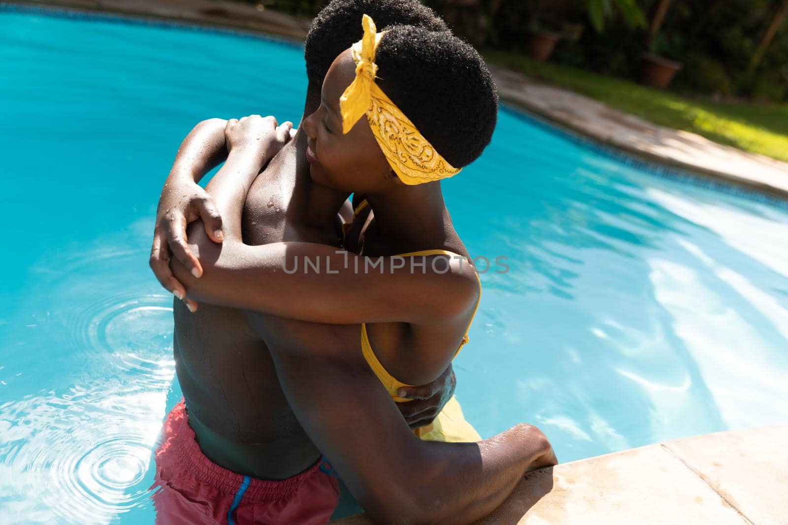 African american couple in water embracing by poolside on sunny garden terrace. staying at home in isolation during quarantine lockdown.