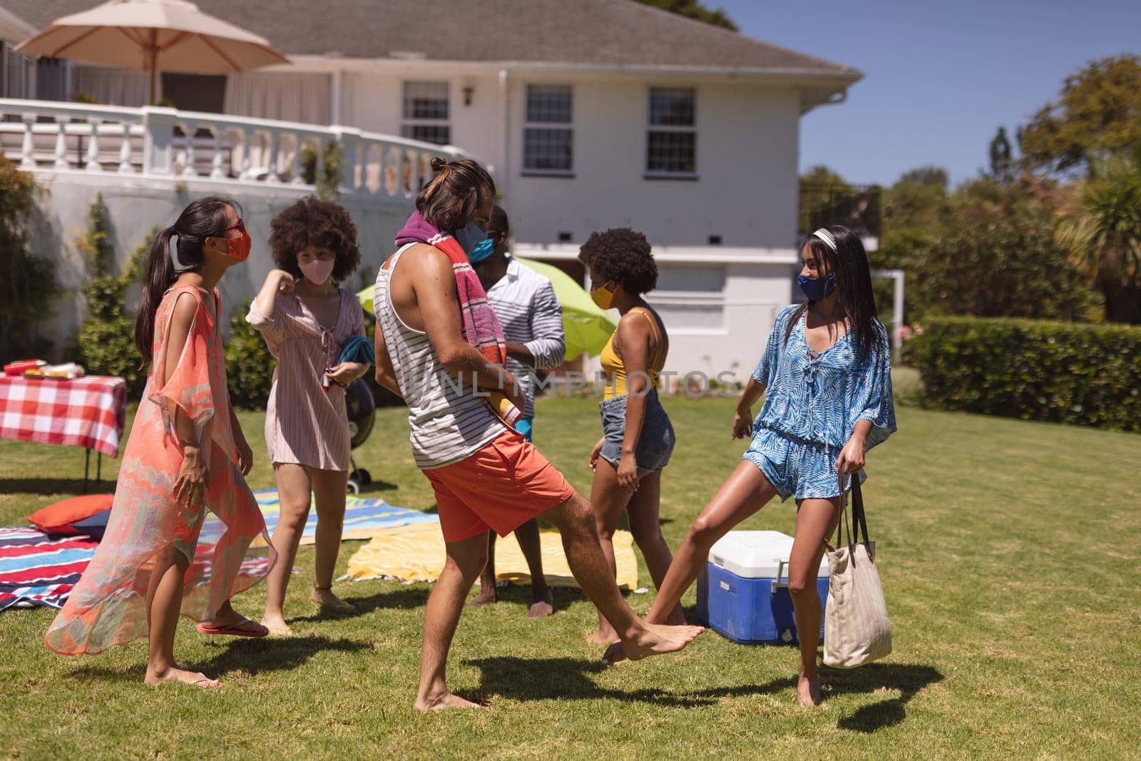 Group of diverse friends wearing face masks bumping legs at a pool party by Wavebreakmedia