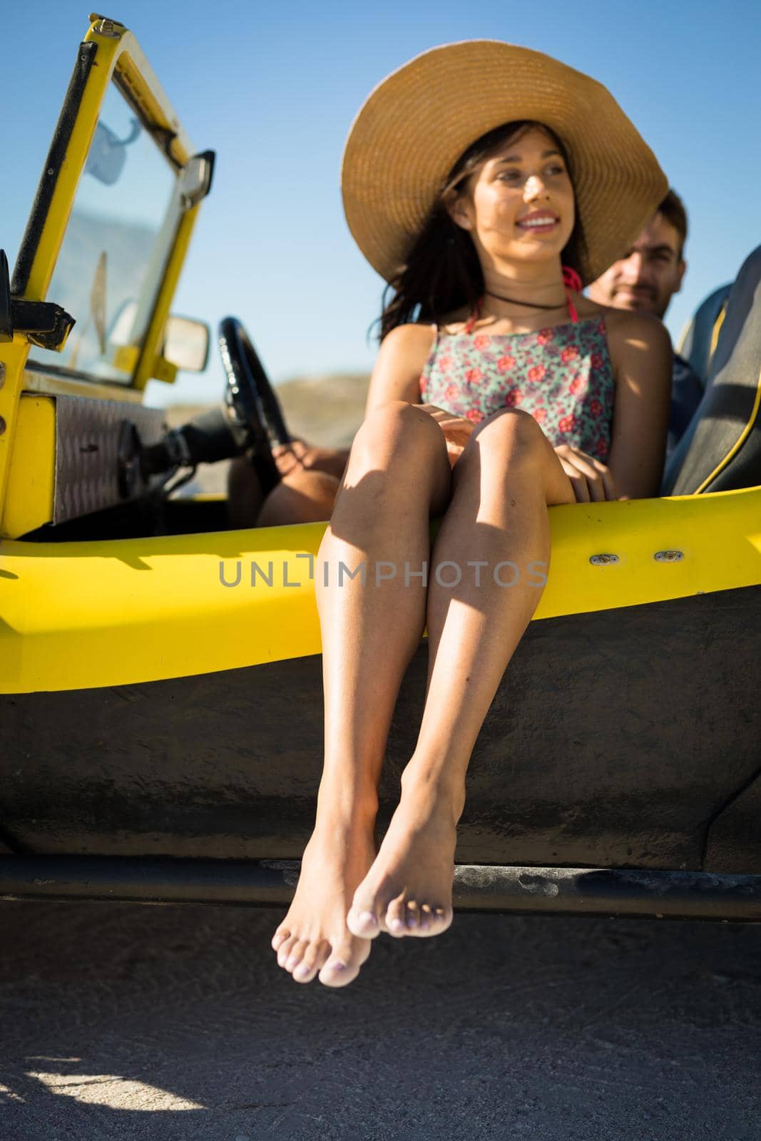 Happy caucasian couple sitting in beach buggy by the sea wearing straw hat. beach break on summer holiday road trip.