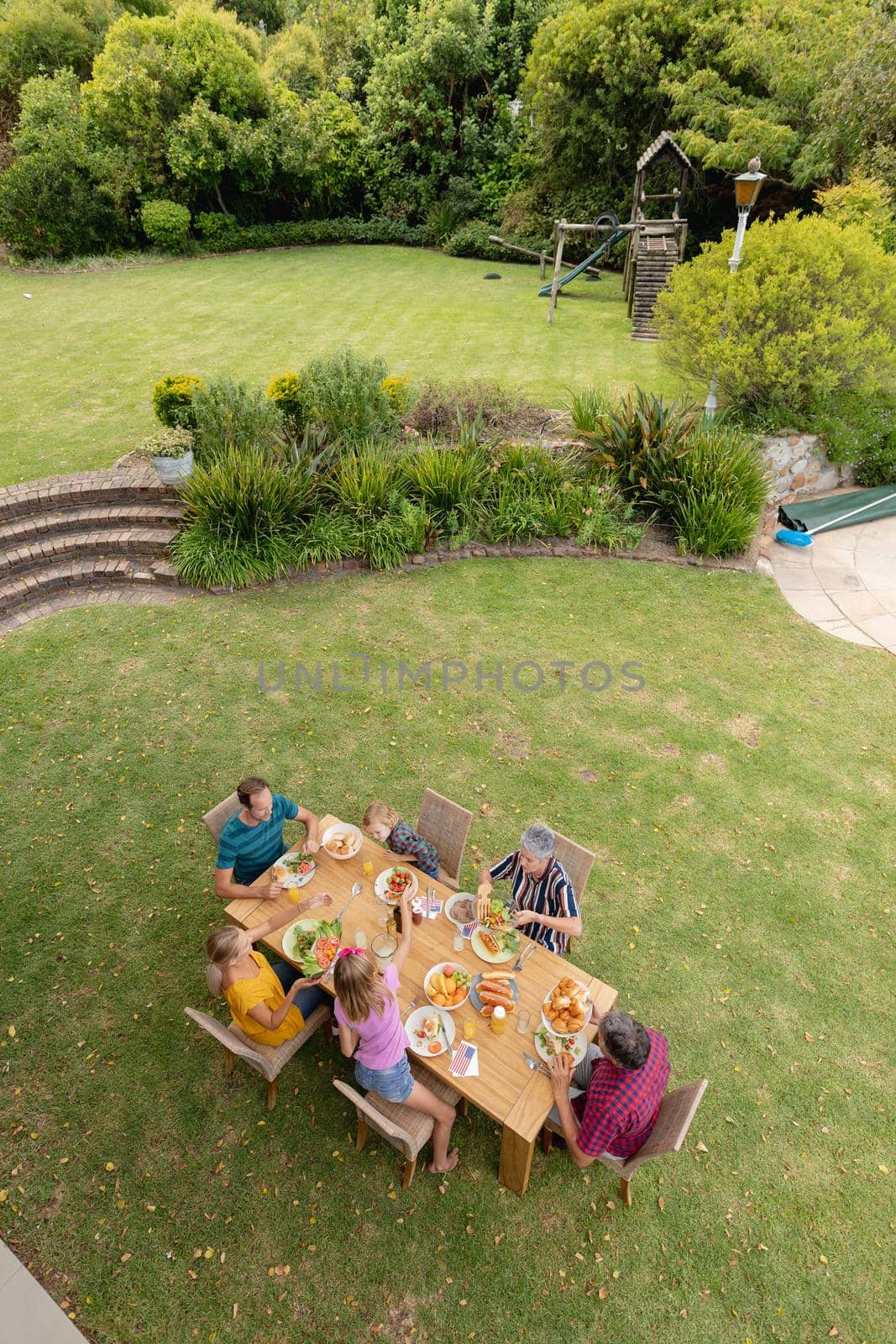 High angle view of caucasian three generation family sitting at table eating meal in garden. three generation family celebrating eating outdoors together.