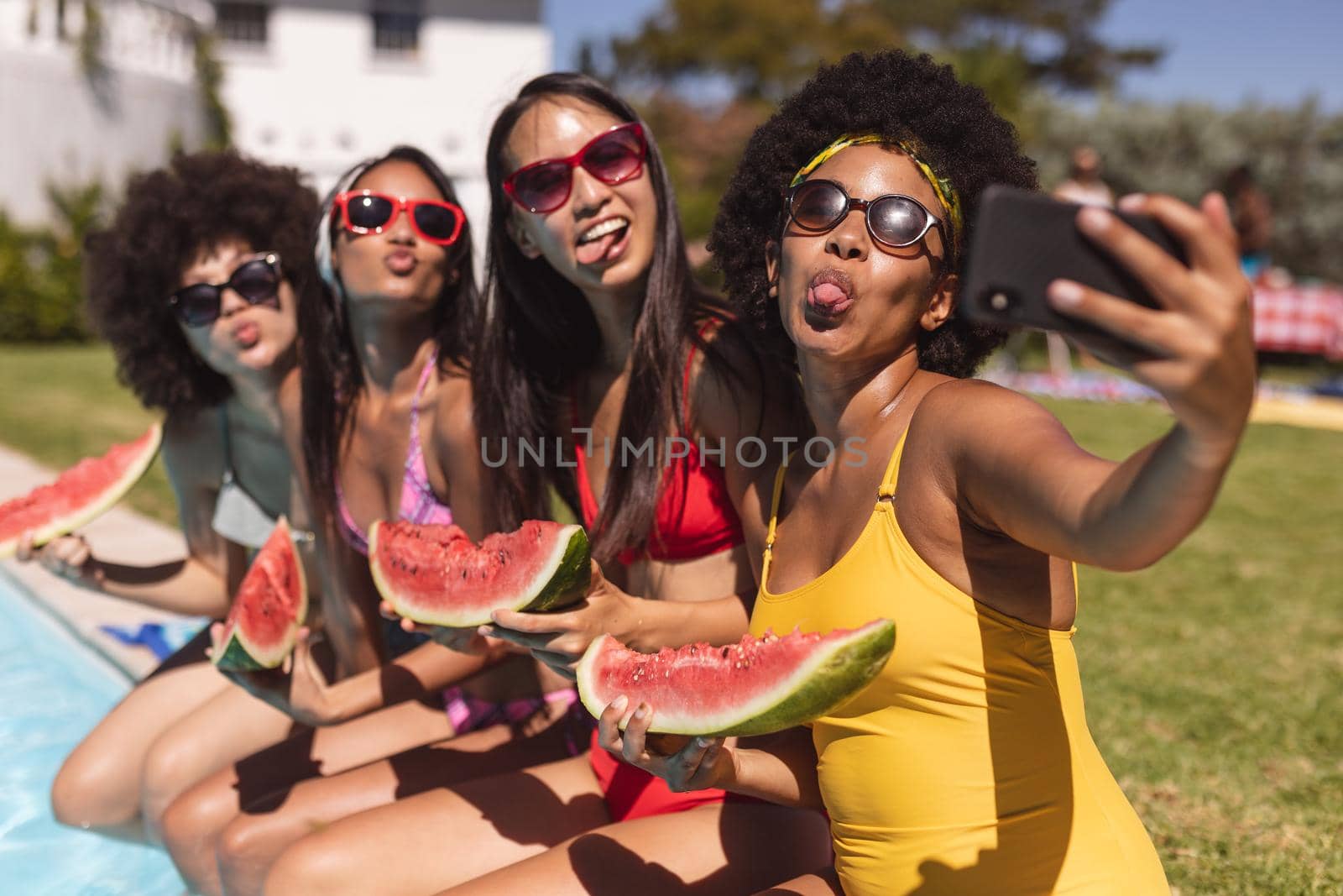 Diverse group of female friends taking selfie with watermelon sitting at the poolside by Wavebreakmedia