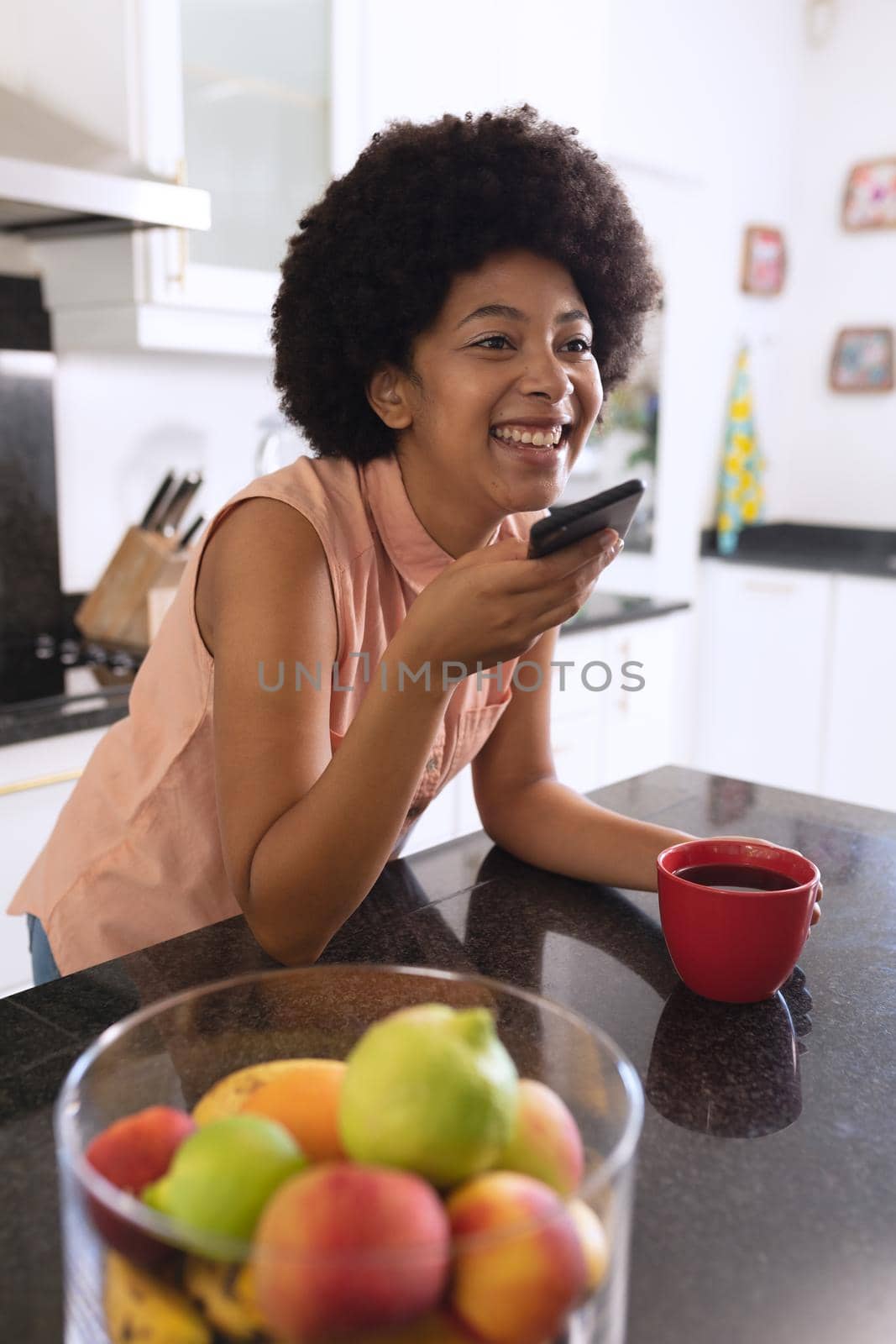 African american woman in kitchen drinking coffee and talking on smartphone. staying at home in isolation during quarantine lockdown.