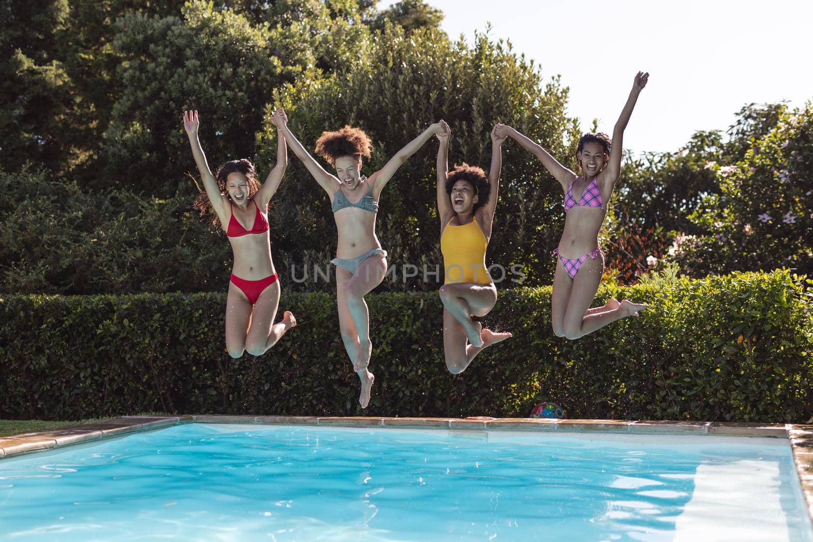 Diverse group of female friends having fun and jumping into water at a pool party. hanging out and relaxing outdoors in summer.