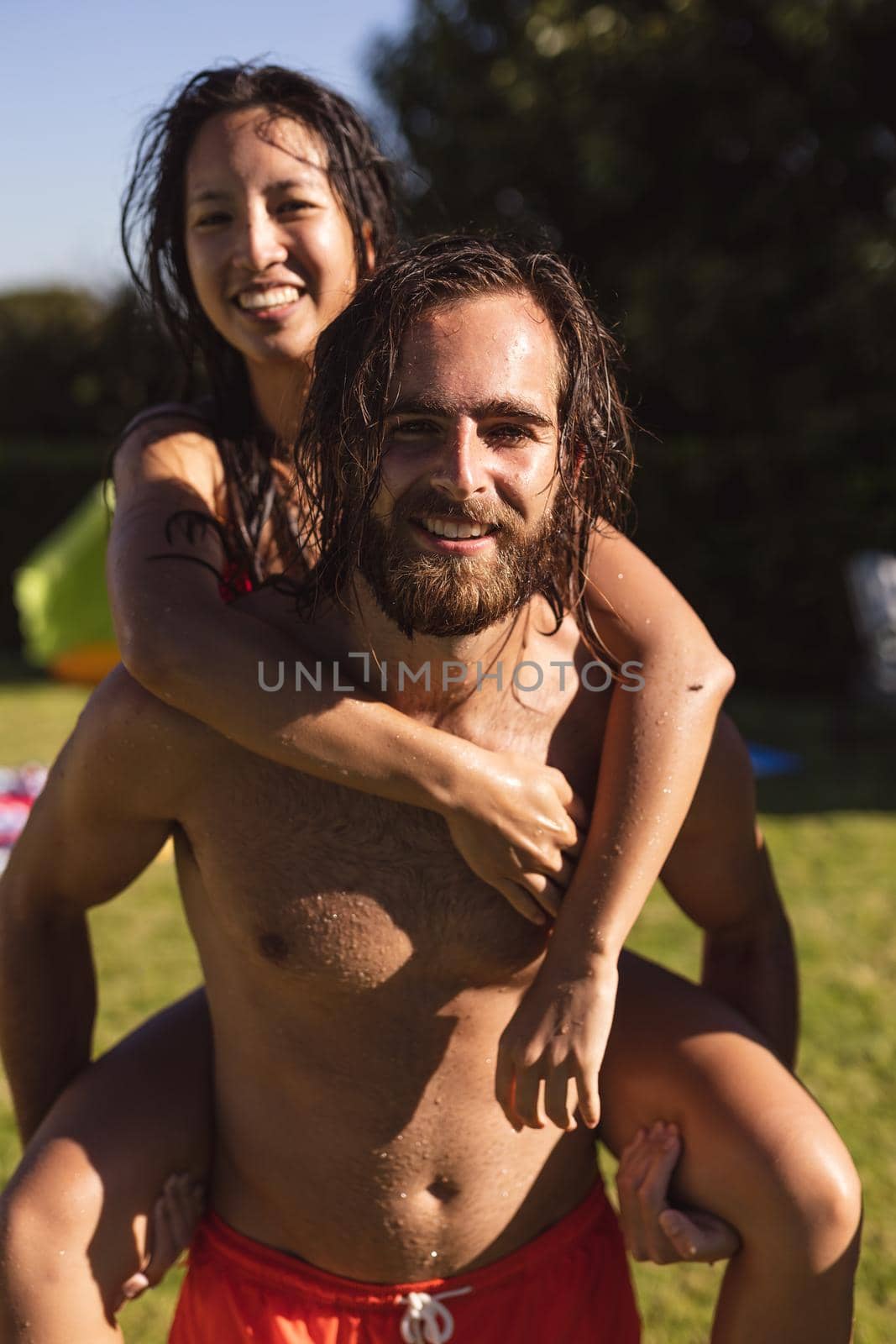 Portrait of two diverse male and female friends man carrying on back and smiling. hanging out and relaxing outdoors in summer.