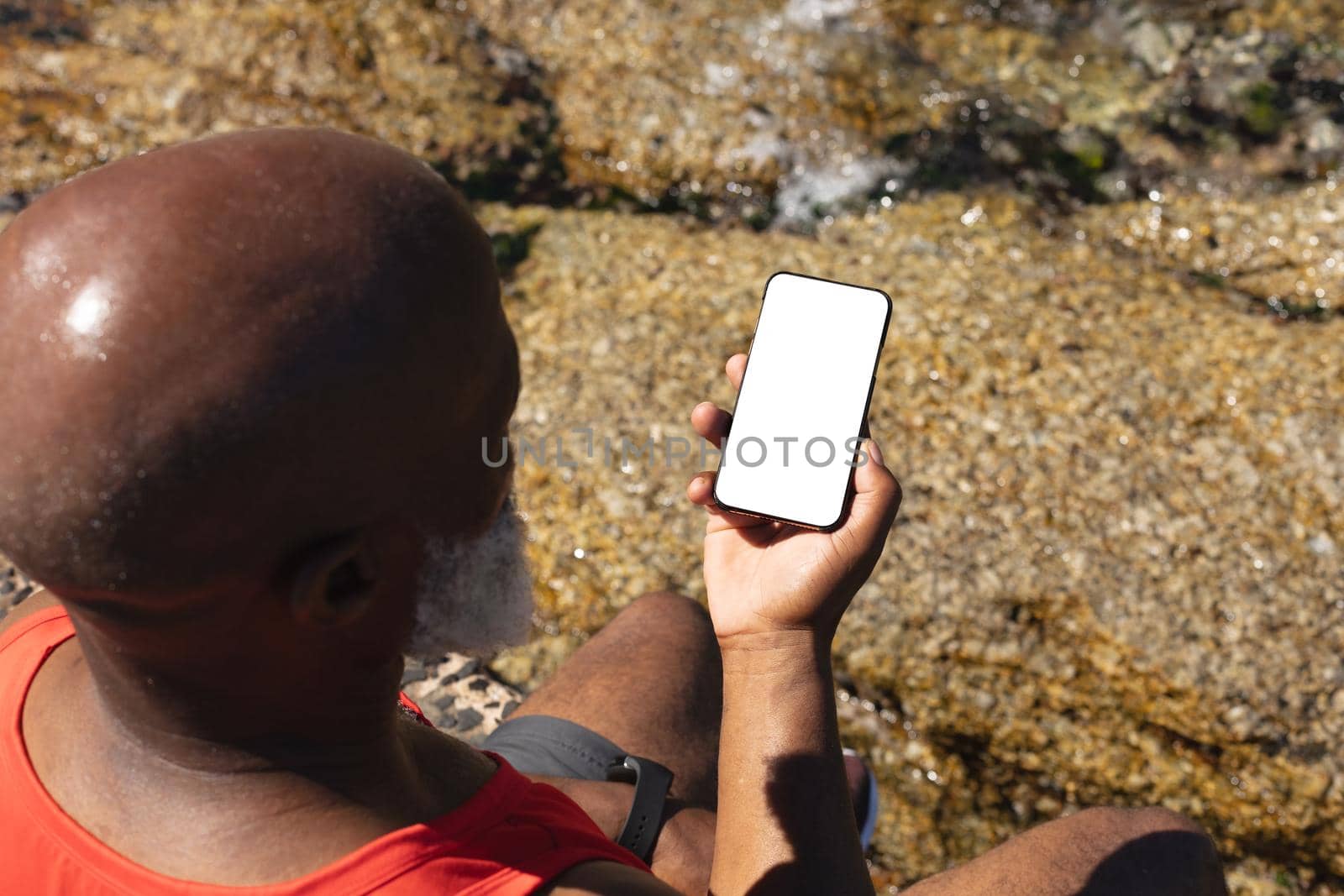 Senior african american man using smartphone by the sea. healthy retirement technology communication outdoor fitness lifestyle.