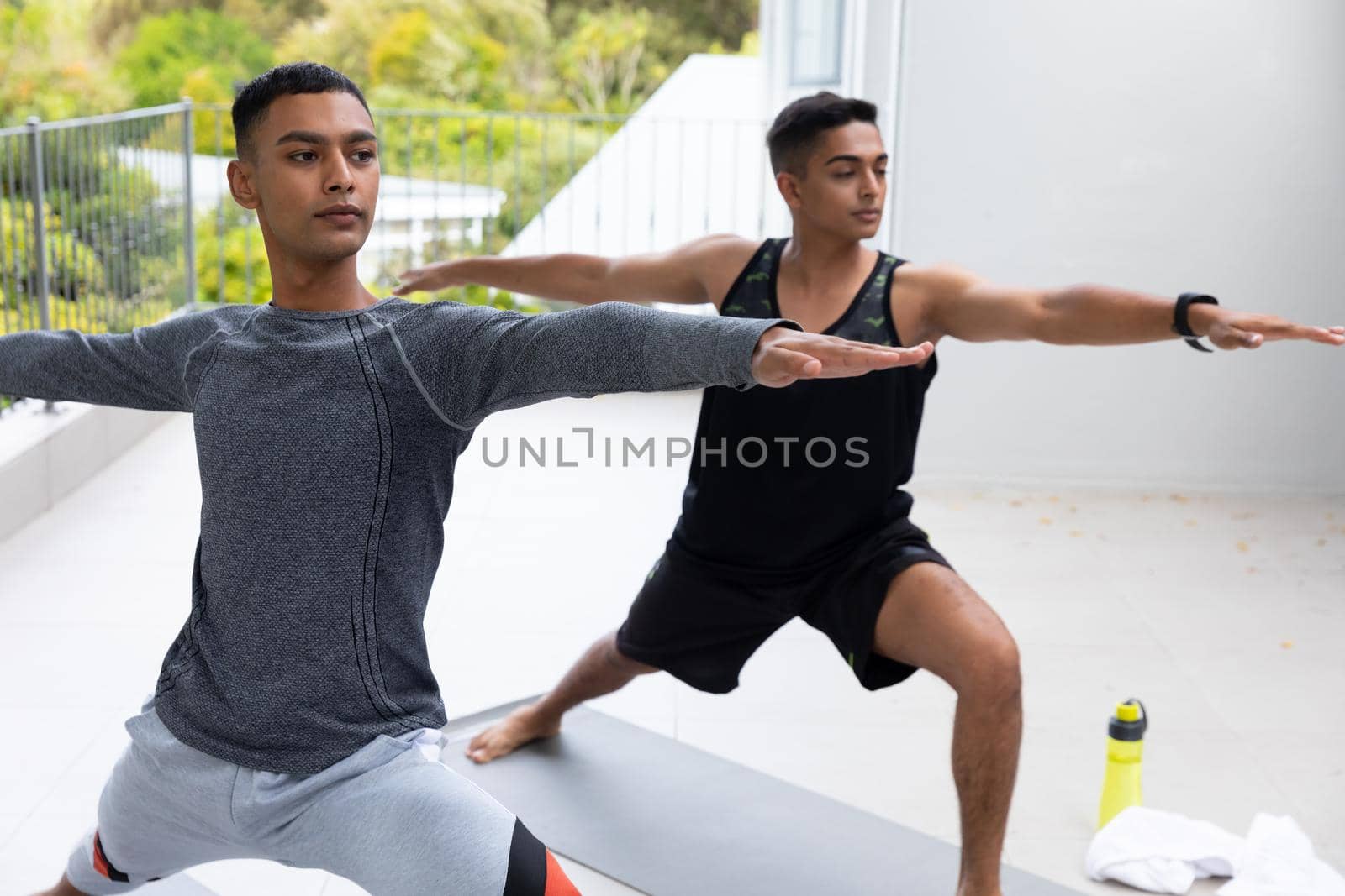 Diverse gay male couple practicing yoga on balcony. staying at home in isolation during quarantine lockdown.