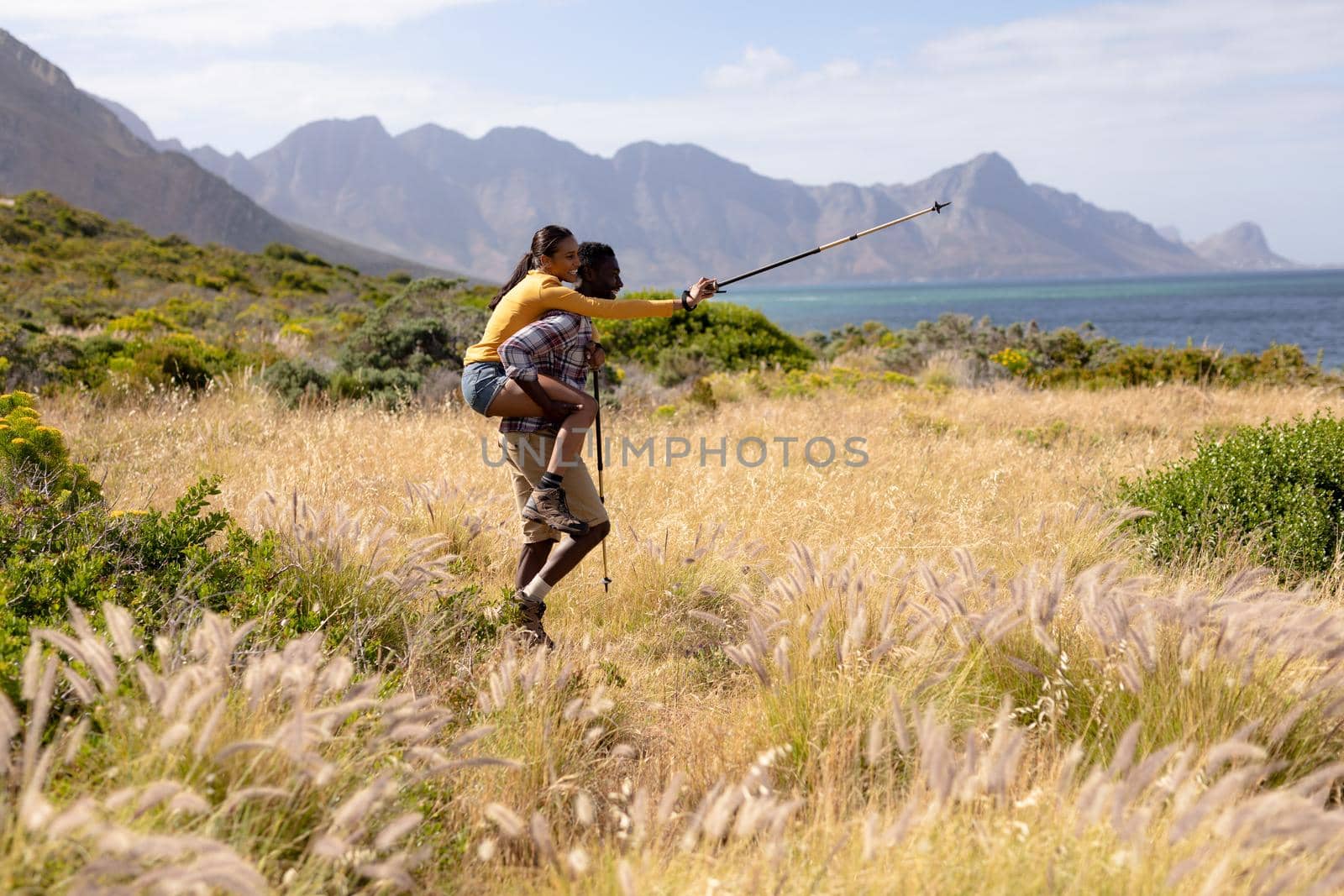 Fit african american couple playing with poles and embracing in mountain countryside. healthy lifestyle, exercising in nature.