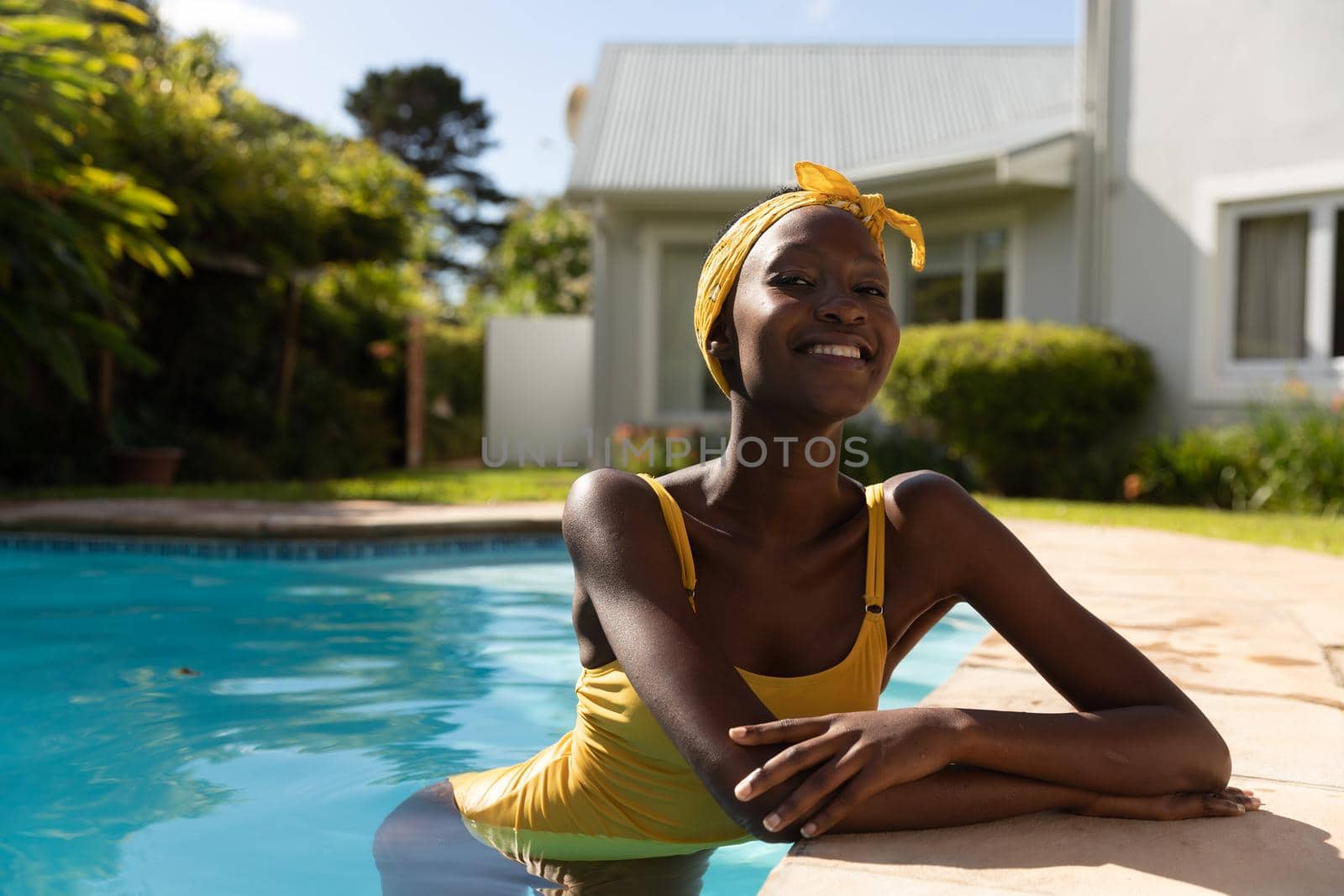 Portrait of african american woman in water leaning on poolside on sunny garden terrace. staying at home in isolation during quarantine lockdown.