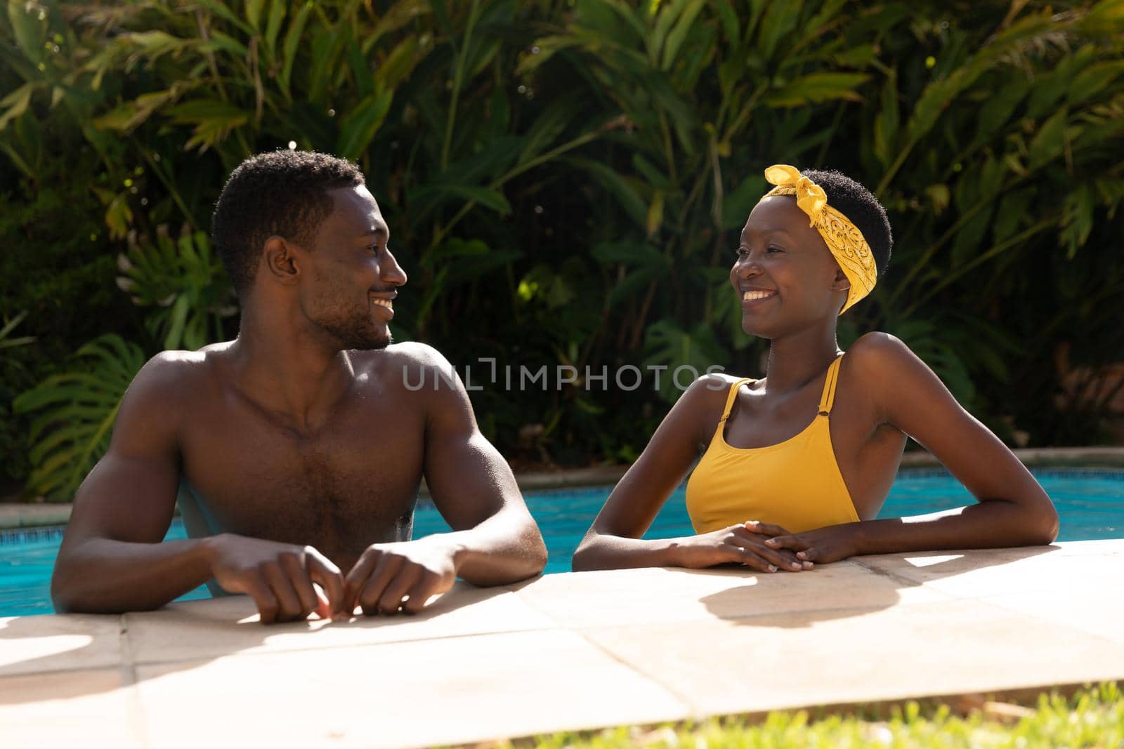 African american couple in water leaning on poolside on sunny garden terrace by Wavebreakmedia