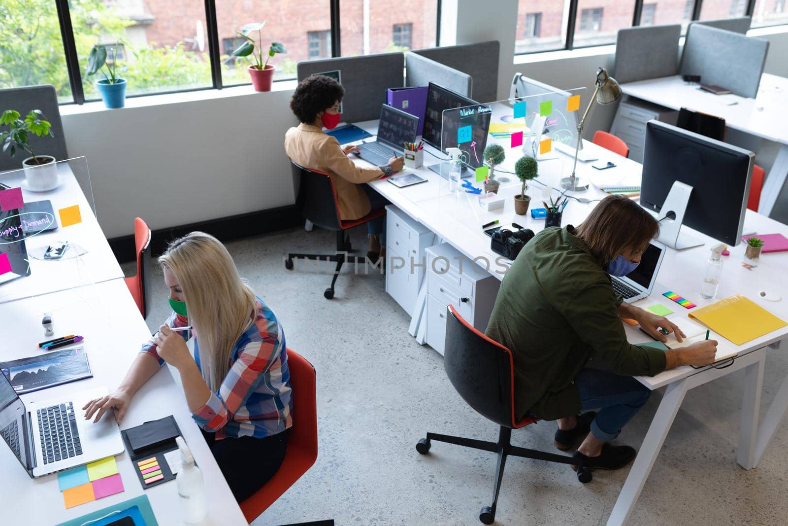 Diverse group of business people wearing face masks in creative office by Wavebreakmedia