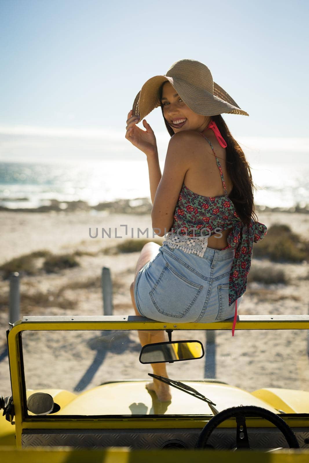 Happy caucasian woman sitting on beach buggy by the sea wearing straw hat looking to camera by Wavebreakmedia