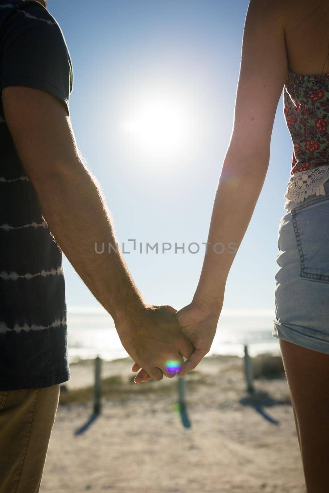 Midsection of caucasian couple on beach holiday holding hands by Wavebreakmedia
