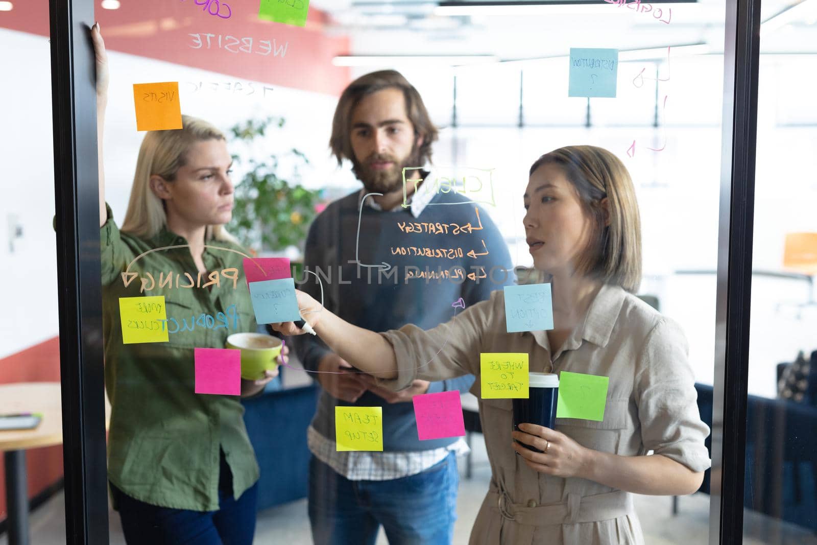 Diverse group of business people working in creative office. group of people brainstorming and taking notes on glass board. business people and work colleagues at a busy creative office.