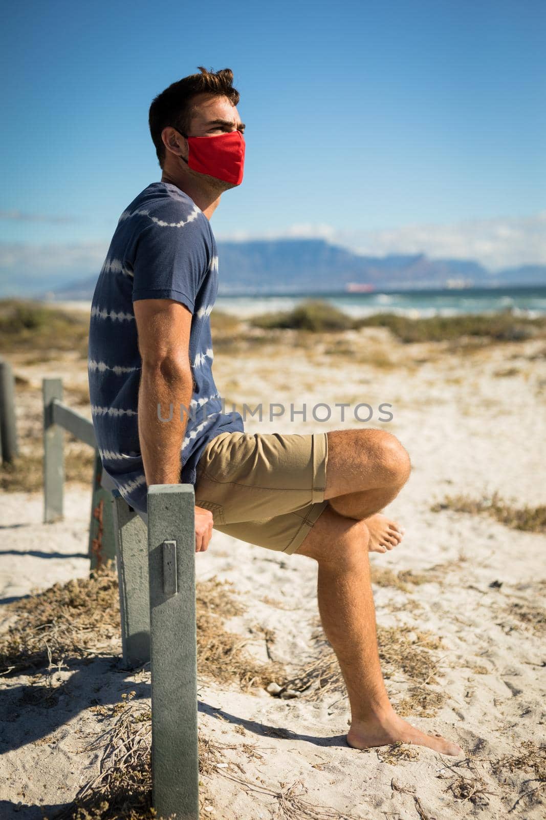Caucasian man wearing face masks sitting on beach by the sea by Wavebreakmedia