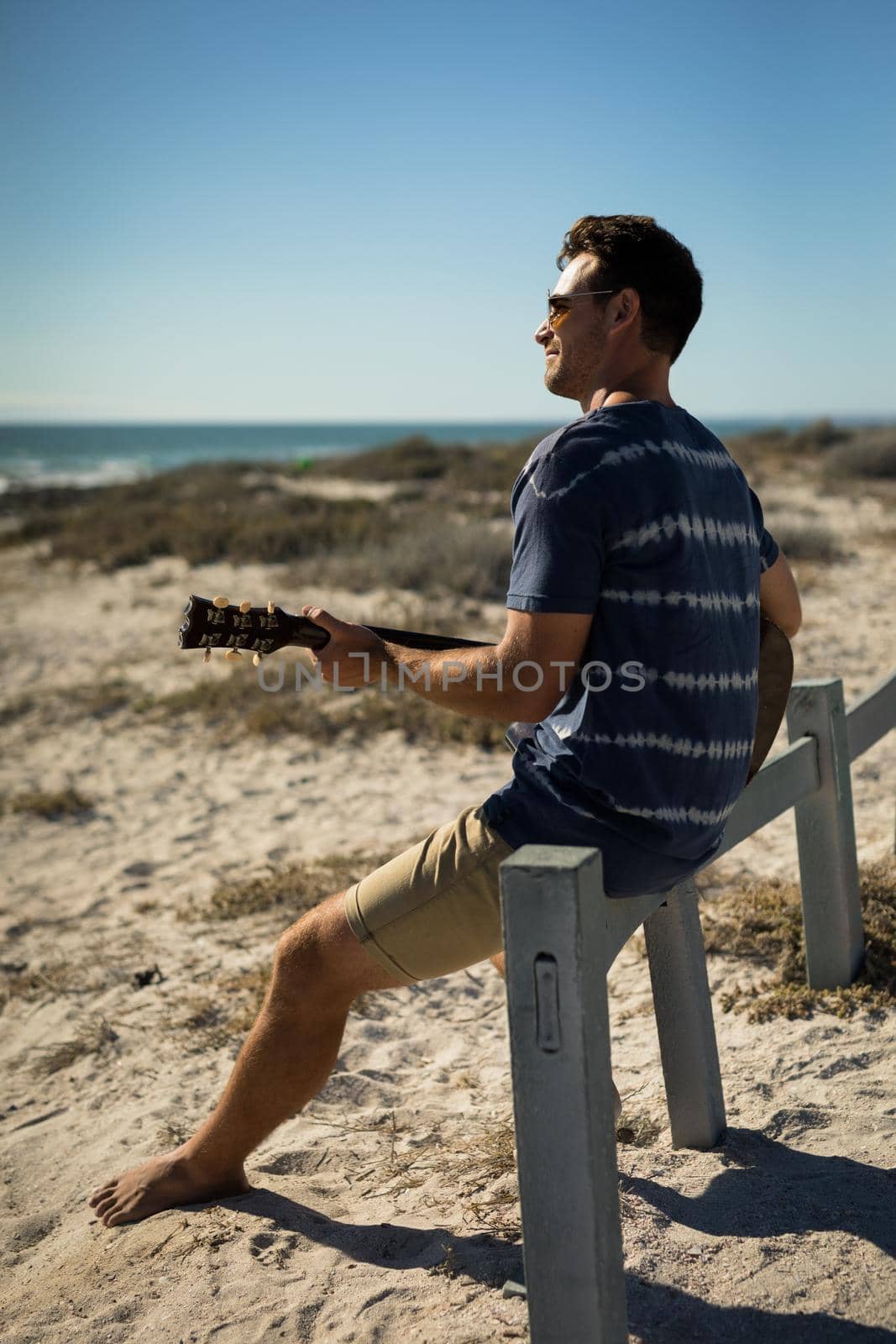 Happy caucasian man sitting on beach by the sea playing guitar. healthy outdoor leisure time by the sea.