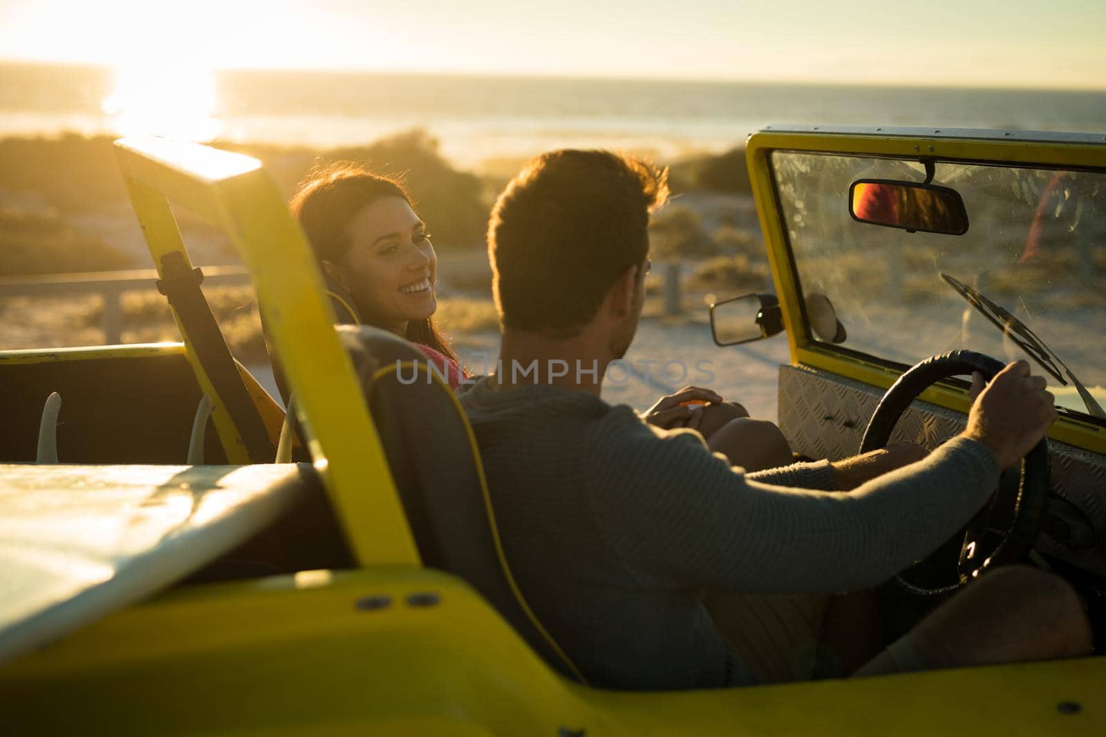 Happy caucasian couple sitting in beach buggy by the sea during sunset. beach break on summer holiday road trip