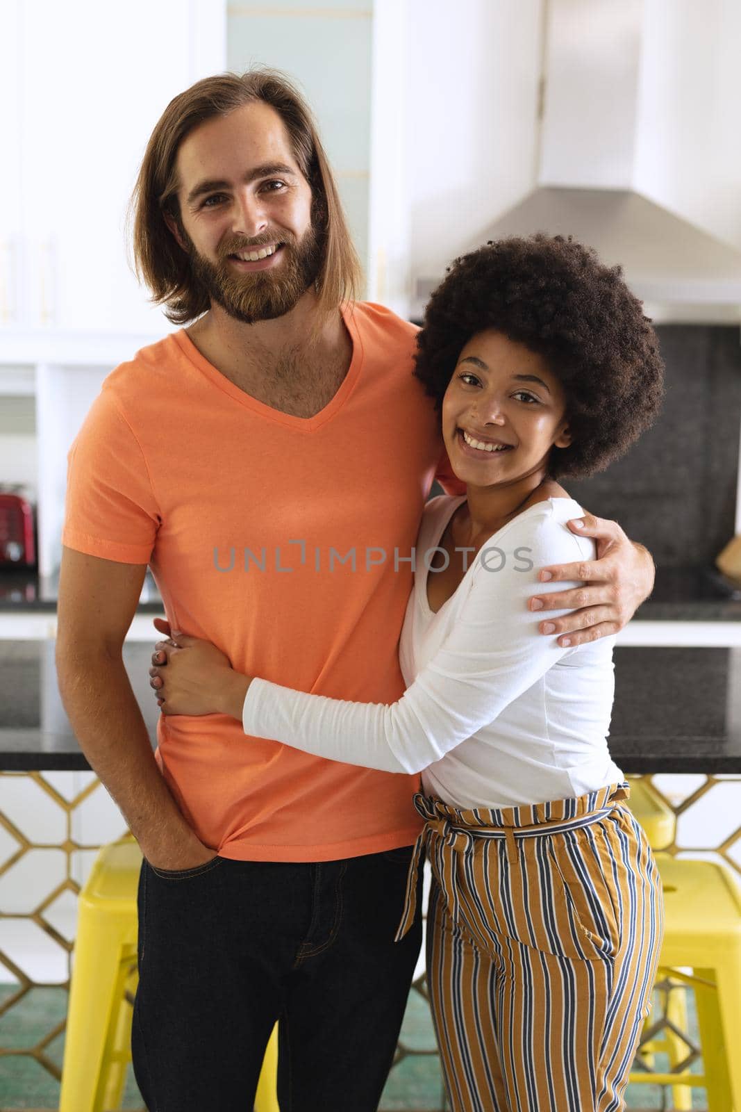 Portrait of happy diverse couple in kitchen smiling and embracing. staying at home in isolation during quarantine lockdown.