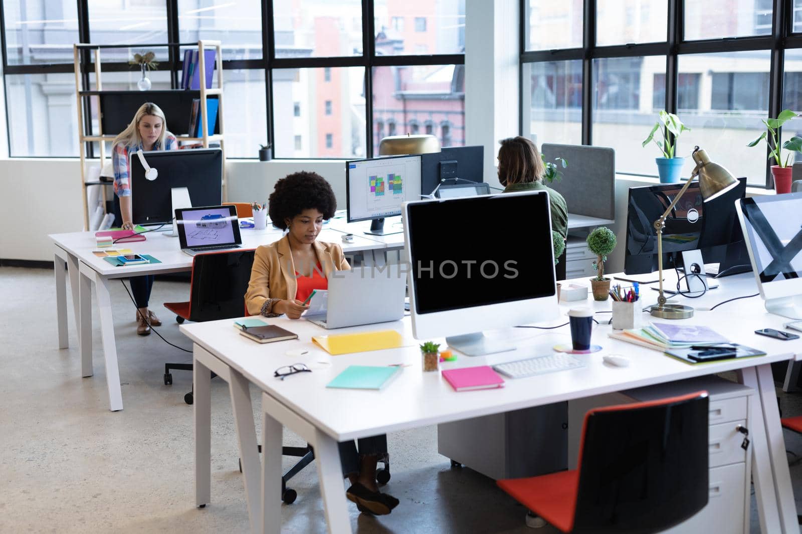 Mixed race businesswoman working in creative office. woman sitting at desk and using laptop computer. social distancing in workplace during covid 19 pandemic.
