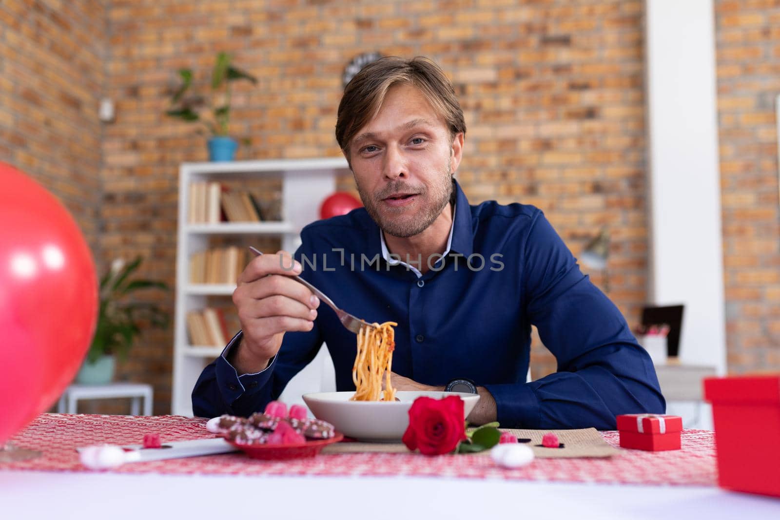 Caucasian man making video call sitting a table eating spaghetti. online communication during quarantine lockdown