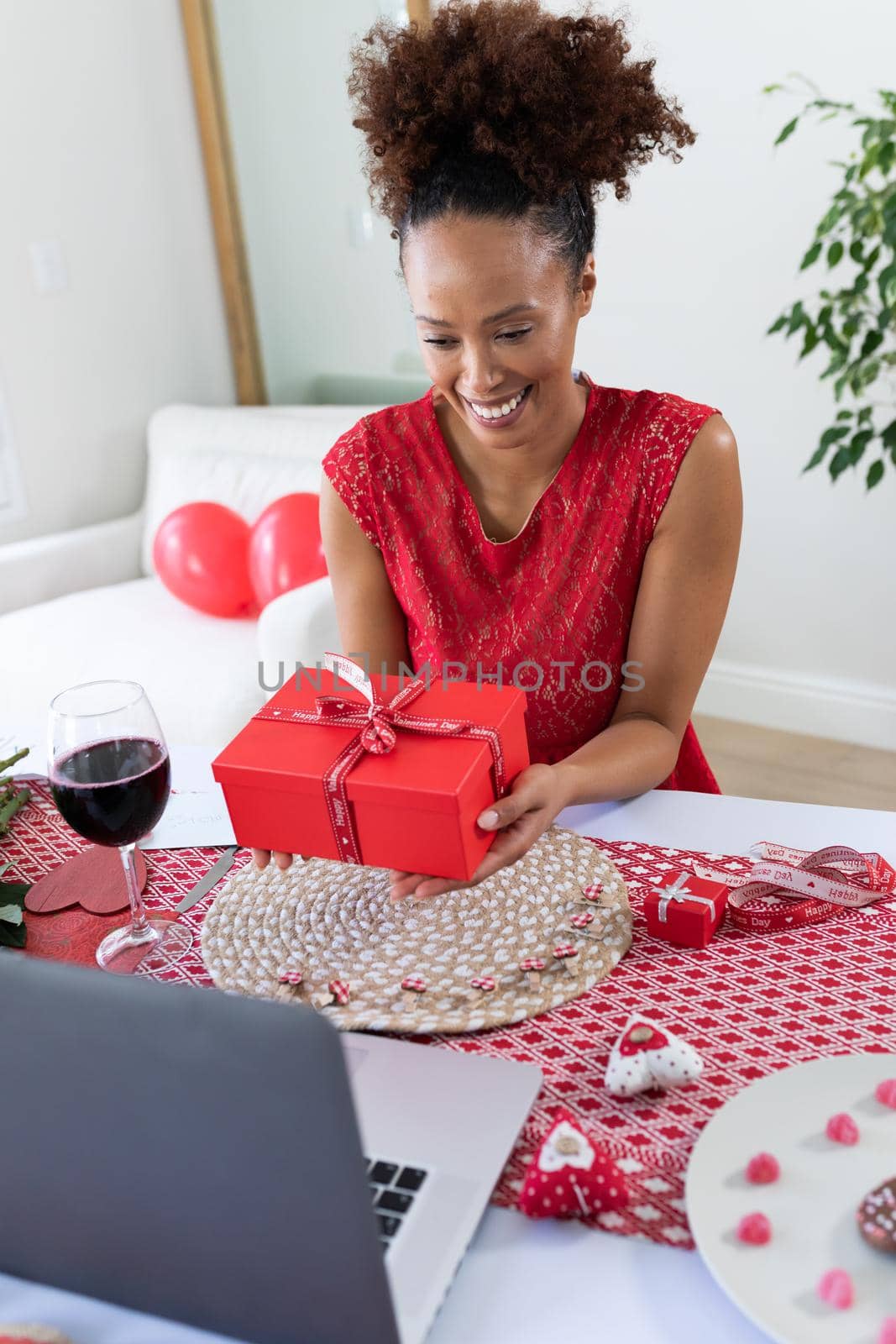 African american woman holding gift box on videocall at home. distant celebration of valentines day online and dating concept
