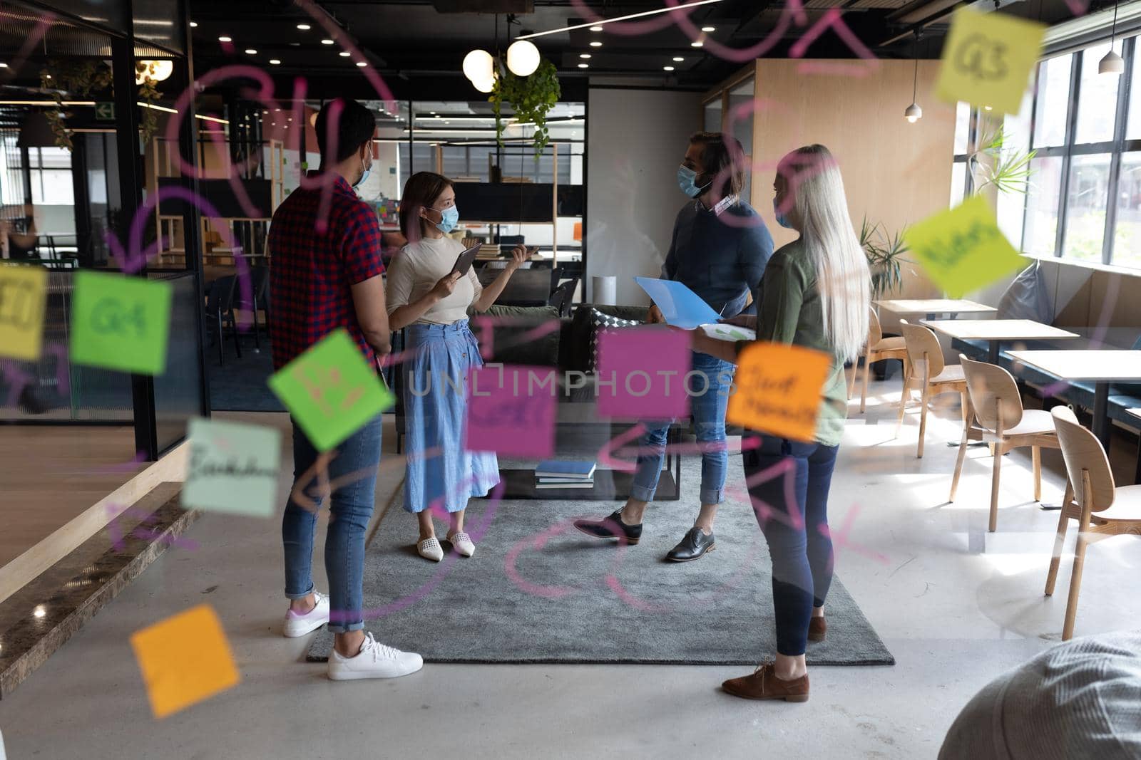 Diverse group of business people working in creative office. group of people wearing face masks and discussing work. social distancing protection hygiene in workplace during covid 19 pandemic.