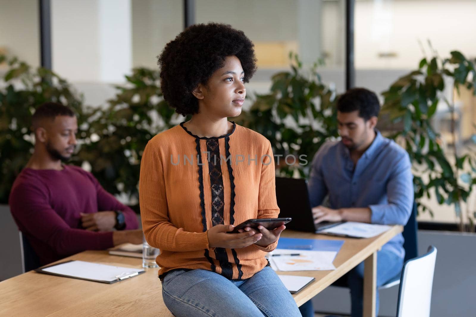 Diverse group of business people working in creative office. woman sitting on a table and using tablet. business people and work colleagues at a busy creative office.