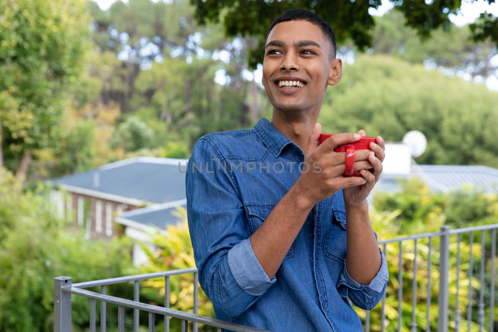 Mixed race man drinking coffee and smiling on balcony. staying at home in isolation during quarantine lockdown.