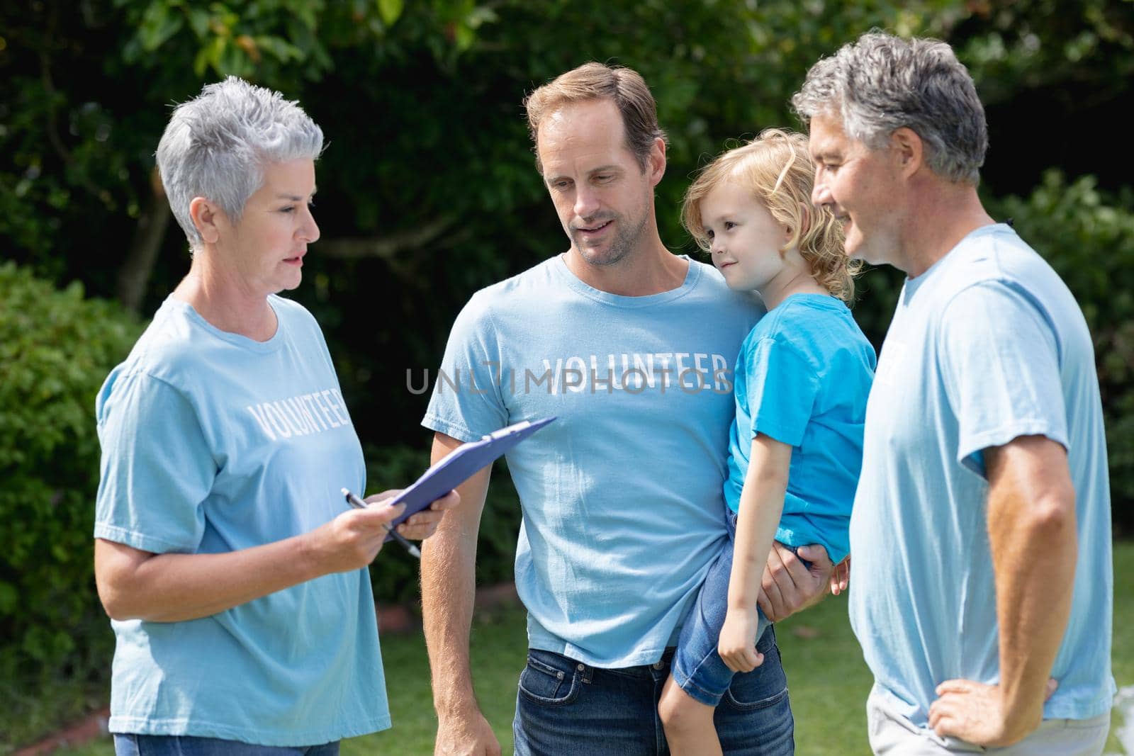 Caucasian senior couple with clipboard and father carrying son in volunteer shirts talking in field. ecology conservation volunteers cleaning up in the countryside.