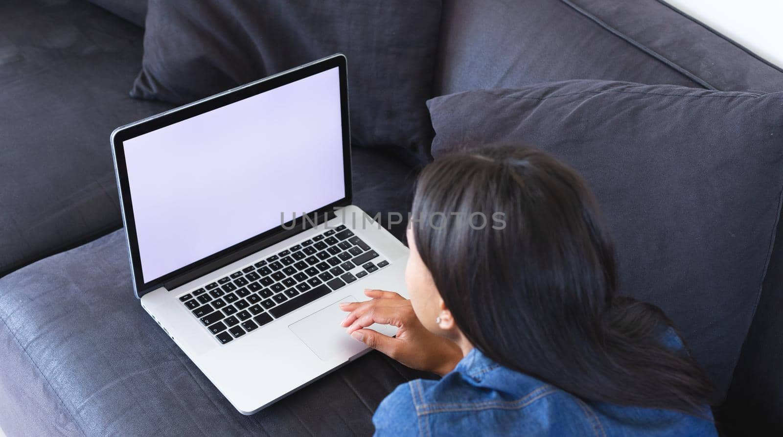 African american woman using laptop with copy space while lying on the couch at home. staying at home in self isolation in quarantine lockdown