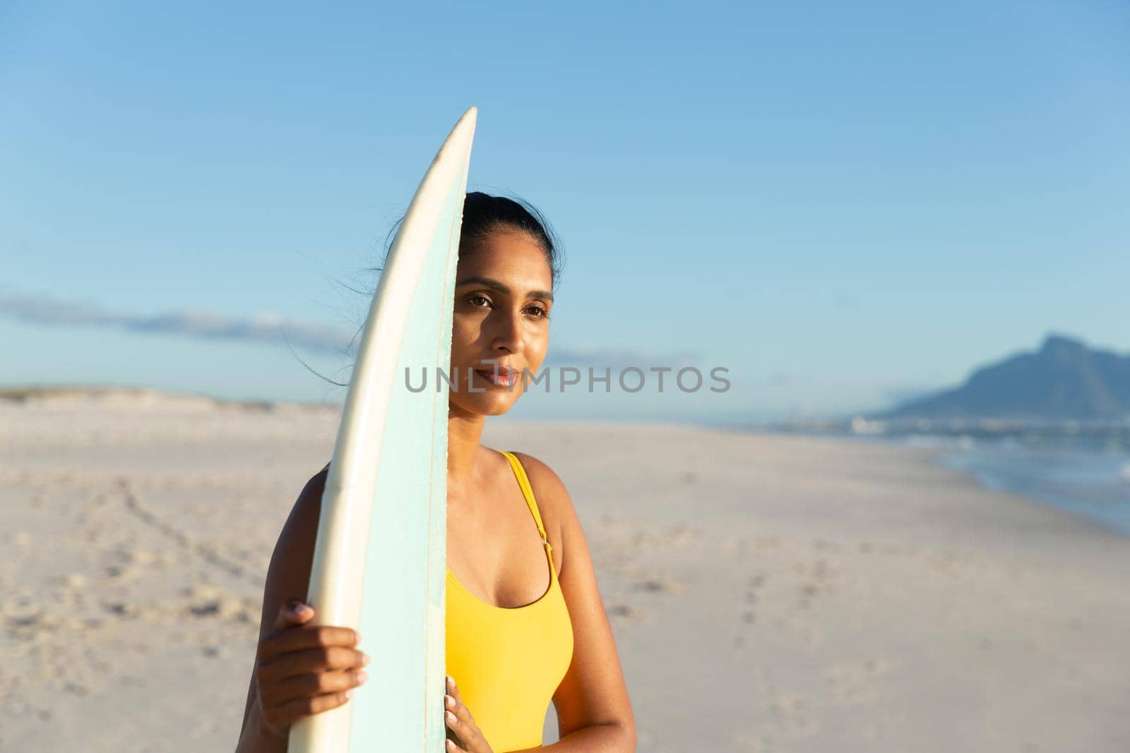 Happy mixed race woman carrying surfboard on the beach by Wavebreakmedia