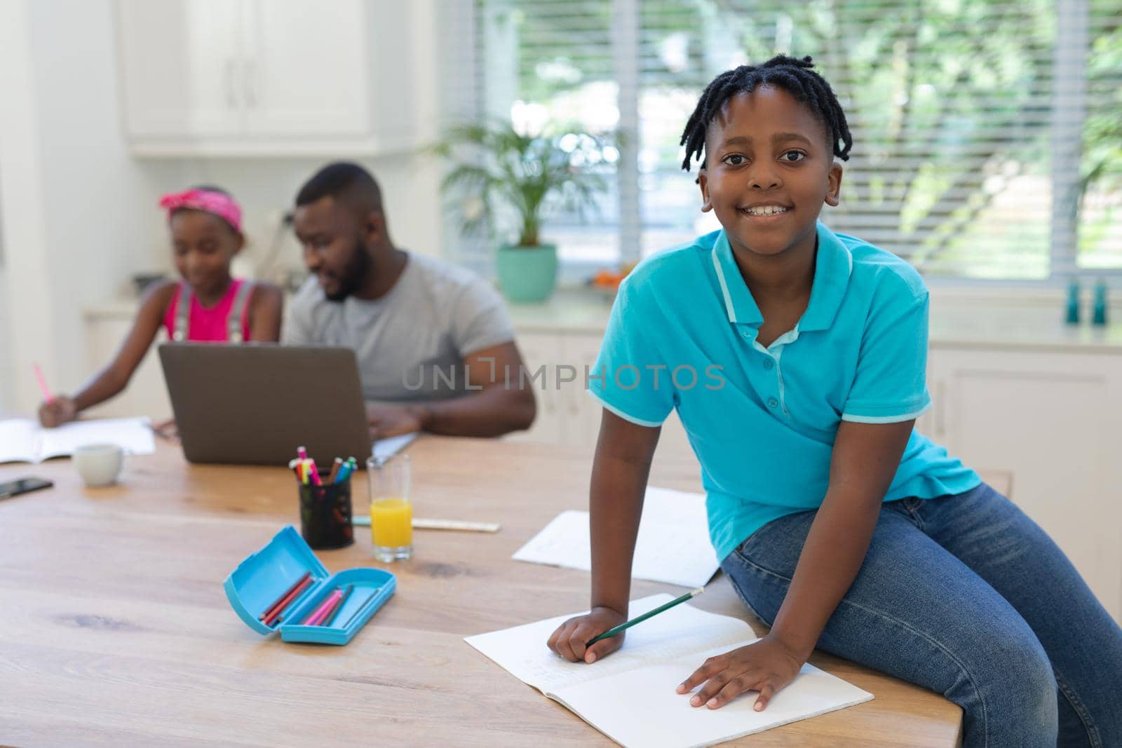 African american boy sitting on counter with father and sister using laptop working from home behind. staying at home in isolation during quarantine lockdown.