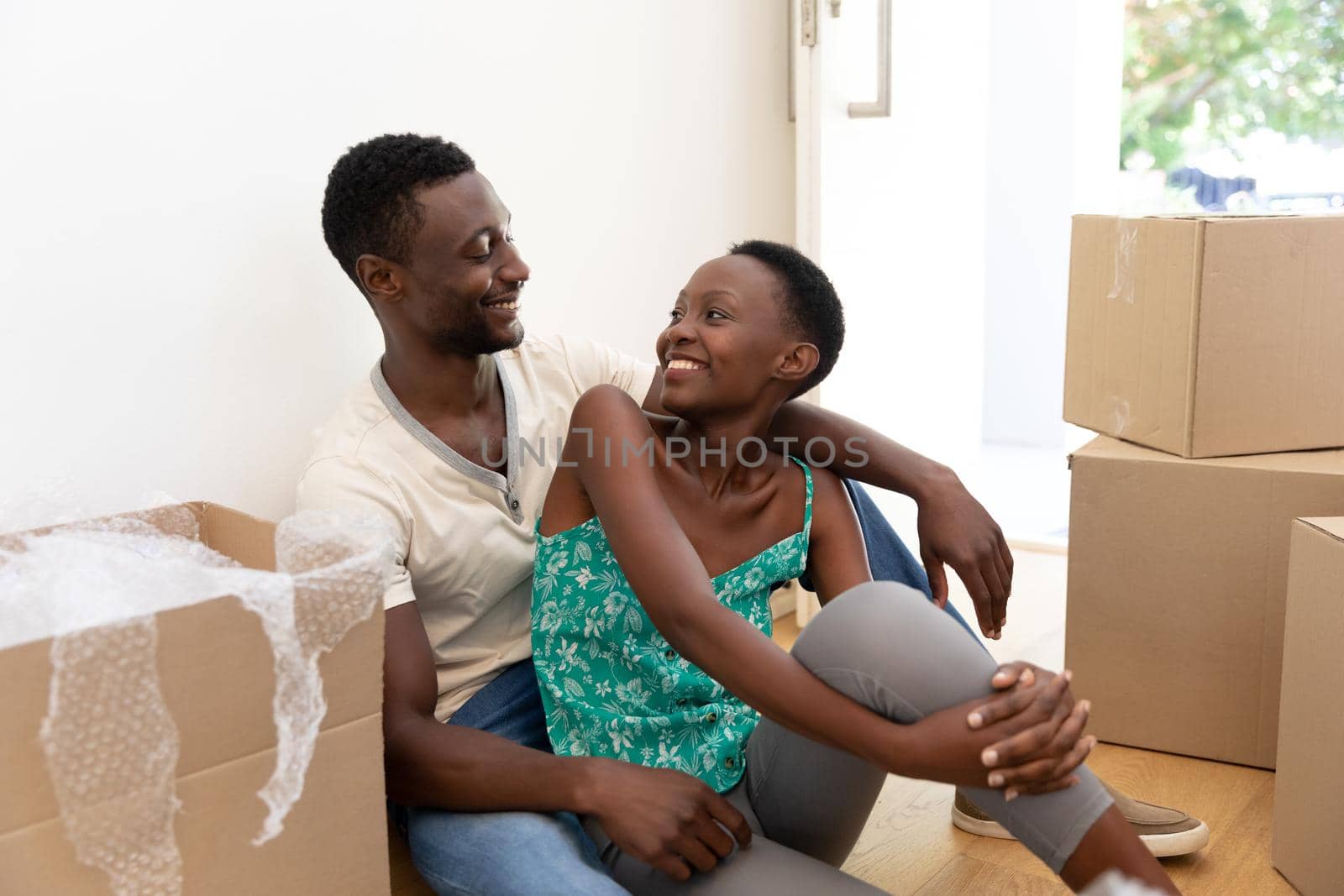 African american couple moving house unpacking sitting on floor and embracing by Wavebreakmedia